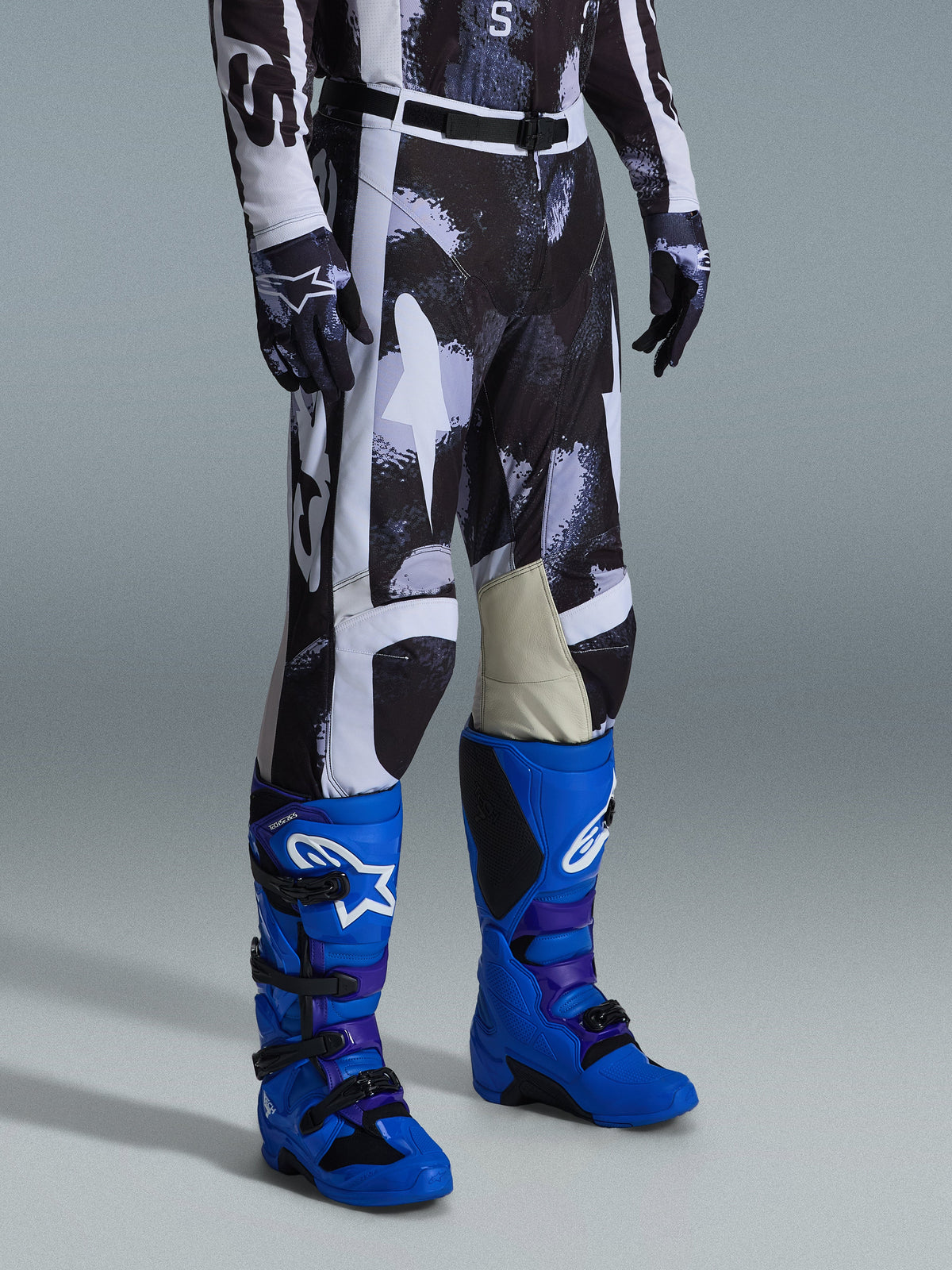 Alpinestars 2026 Racer Lahnd Pants, calças de motocross, padrão camuflado Iron Camo em cinzento e preto, usadas com botas de corrida azul brilhante e luvas a condizer, com painéis brancos e interior dos joelhos em couro de cabra, equipamento de alto desempenho para todo-o-terreno