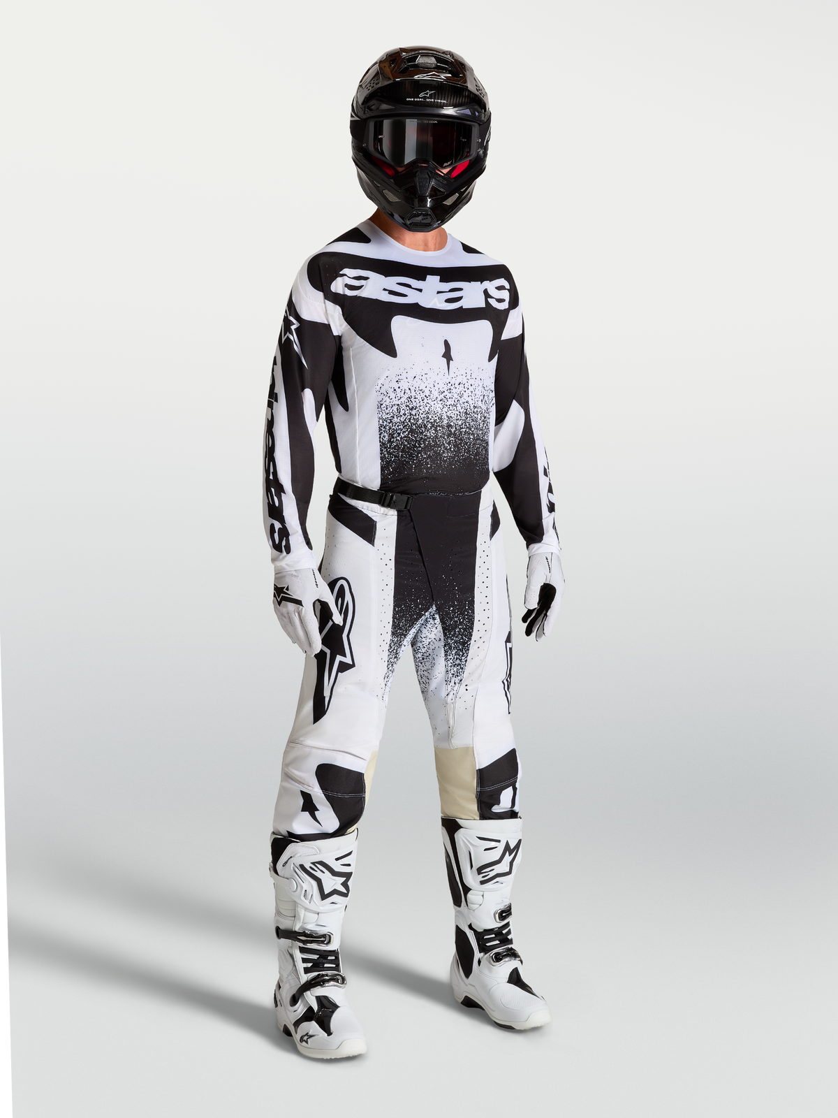 Calças Techstar Swan da Alpinestars, calças de motocross para homem, pretas e brancas, com ajuste atlético e tecido ripstop elástico, modelo vestido com equipamento de todo-o-terreno.