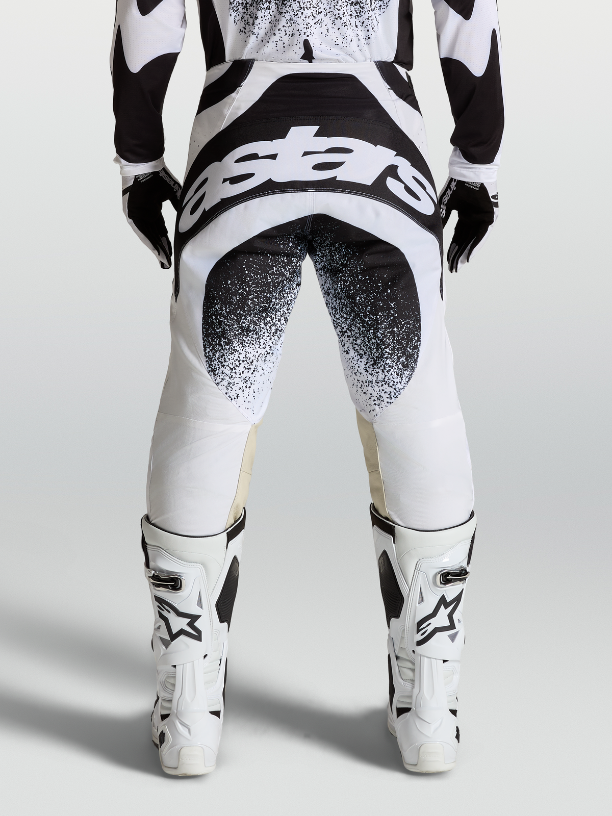 Alpinestars Calças Techstar Swan, calças de motocross profissionais, pretas e brancas, vista traseira com logótipo Astars, construção de joelho Babel.