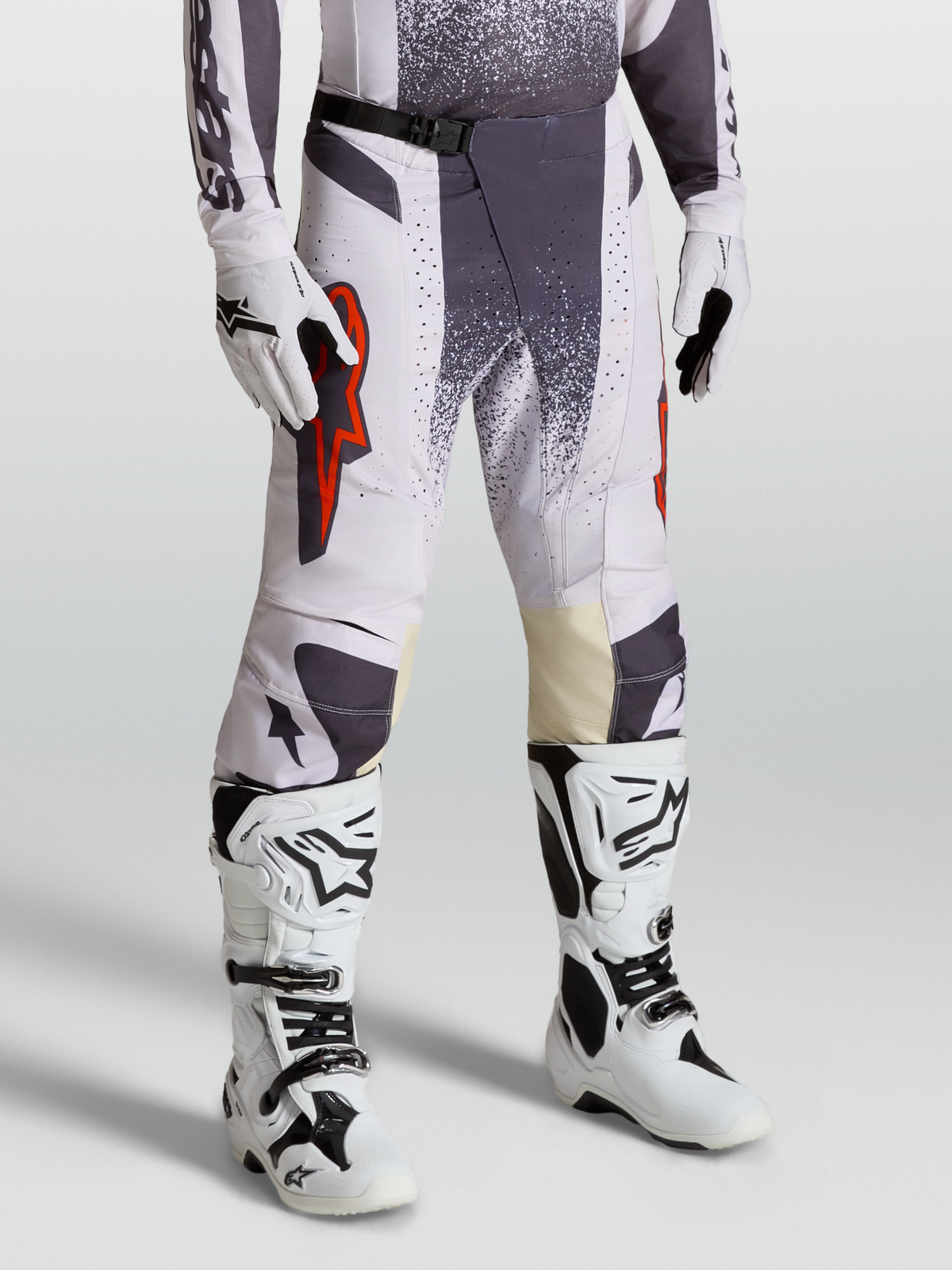 Calças Techstar Swan Alpinestars, calças de motocross para homem, lilás claro e cinzento escuro com detalhes em vermelho fluo, modelo equipado com luvas e botas.