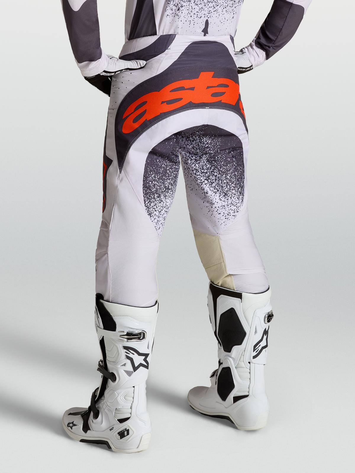 Alpinestars Calças Techstar Swan, calças de motocross para homem, cinzento e lilás com detalhes em vermelho fluo, vista traseira com botas Tech 10