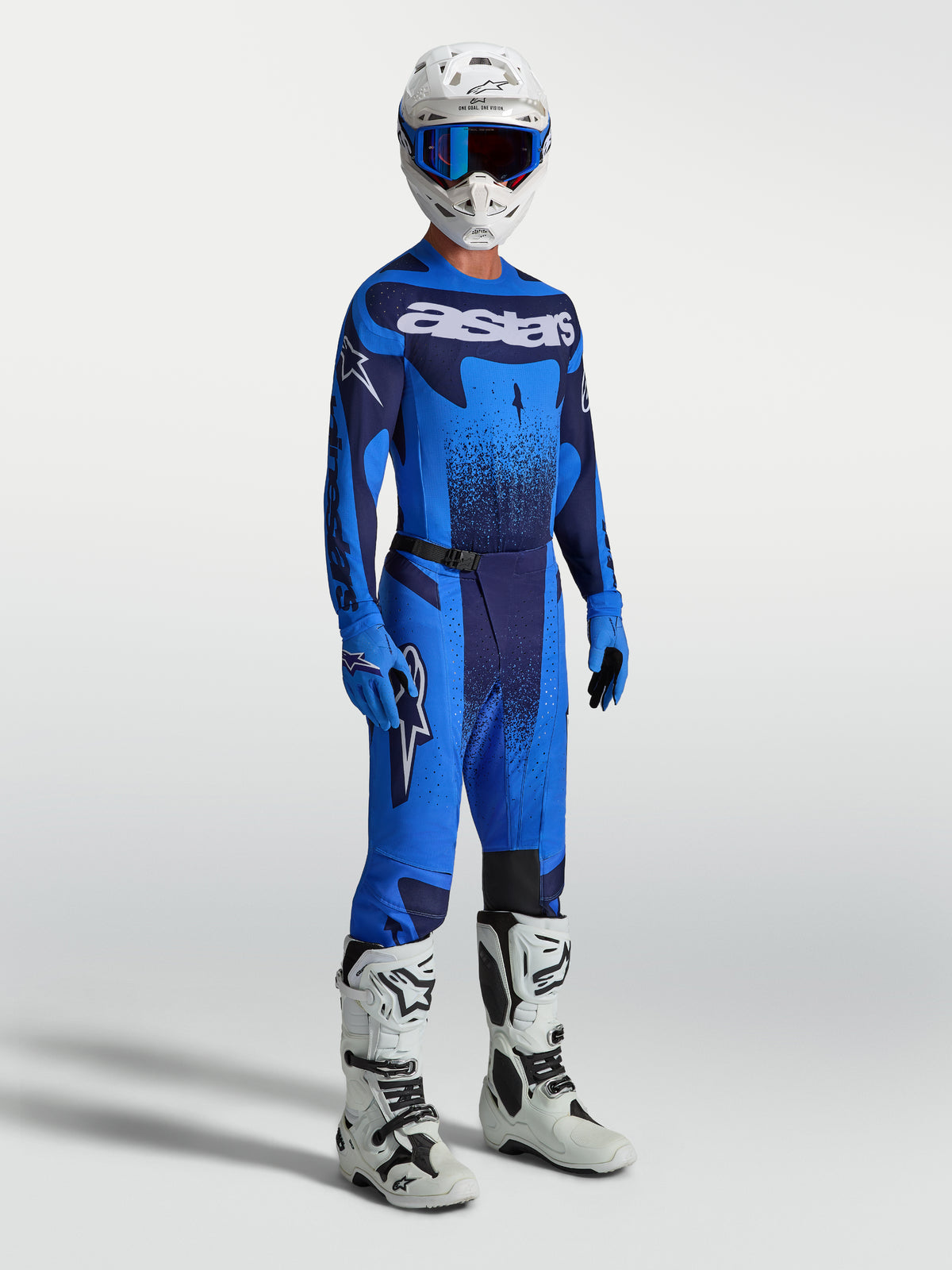 Alpinestars Calças Techstar Swan, calças de motocross para homem, azuis e azul-marinho, apresentadas com camisola a condizer, capacete e botas de corrida brancas.