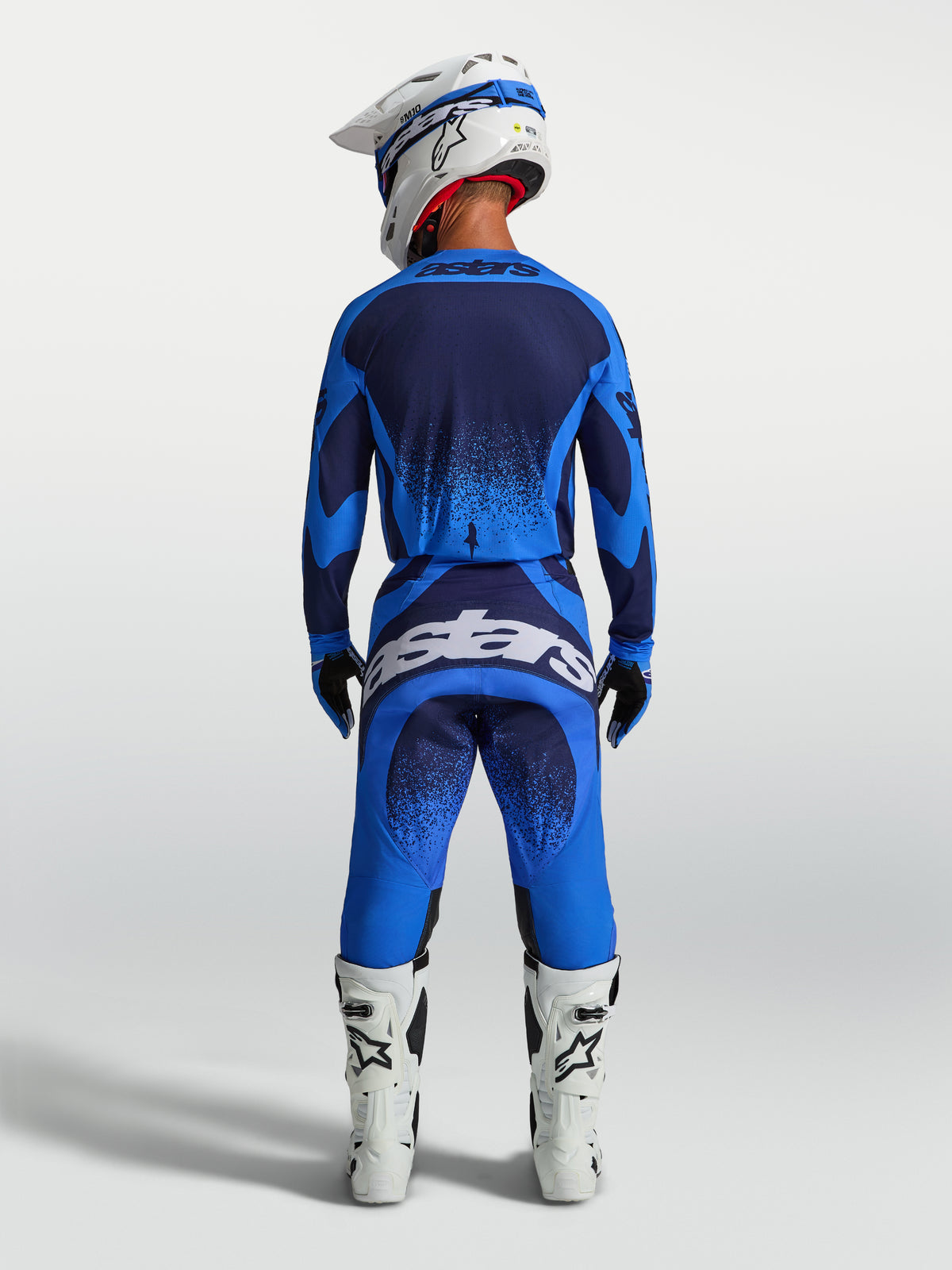 Alpinestars calças Techstar Swan, calças de motocross para homem, azul e azul escuro, vista traseira com botas brancas.