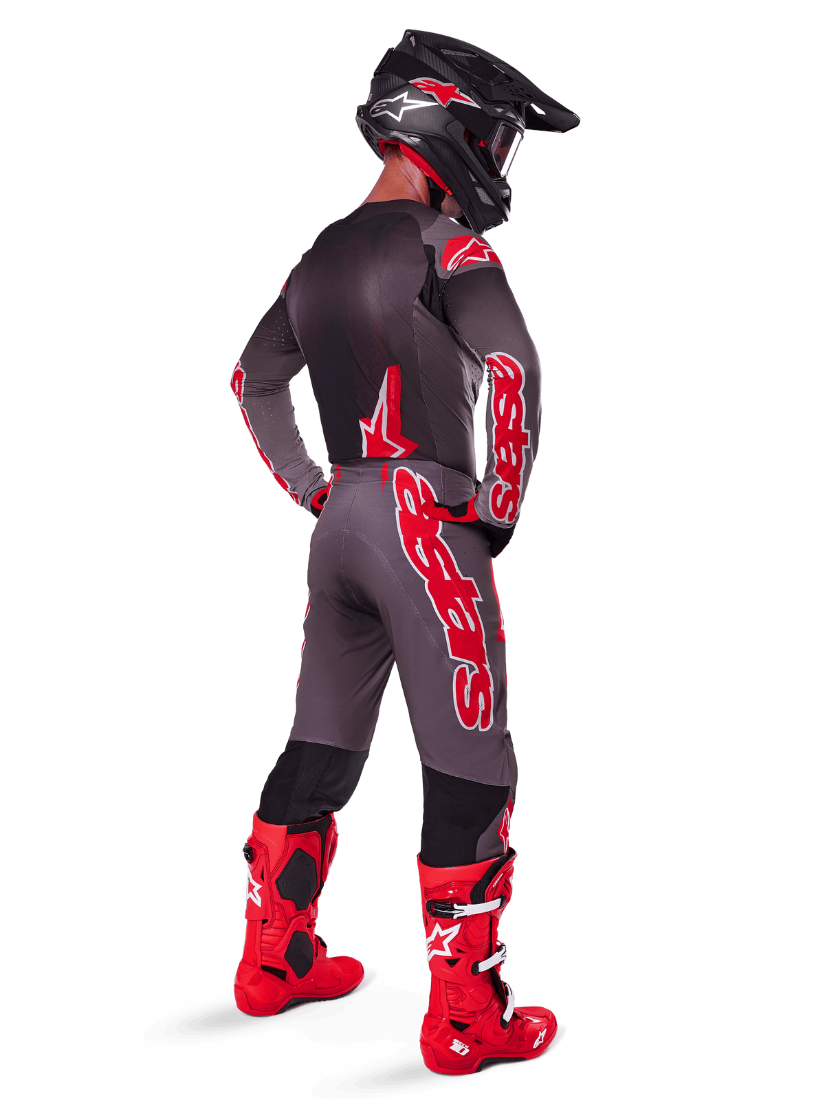 Piloto de motocross com calças Alpinestars 2025 Supertech Lipan, Smoke Bright Red, calças cinzentas com logótipos vermelhos grandes e painéis pretos no interior das pernas, combinadas com camisola cinzenta a condizer, capacete preto e botas vermelho vivo, equipamento completo de corrida todo-o-terreno visto de trás