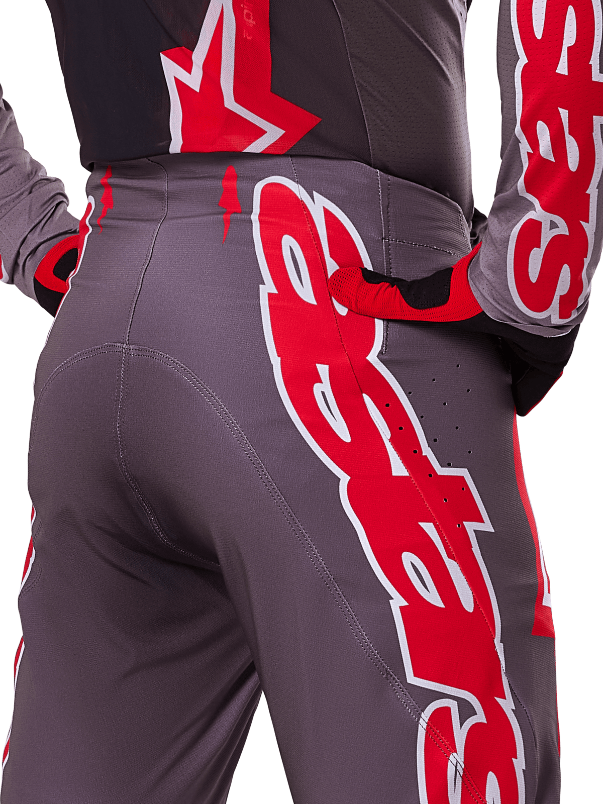 Alpinestars 2025 Supertech Lipan Pants, calças de motocross, Smoke Bright Red, pormenor da vista traseira mostrando o tecido cinzento escuro com grafismos vermelhos vibrantes, usadas com luvas e camisola a condizer em vermelho e preto, com perfurações de ventilação e costuras ergonómicas para performance em todo-o-terreno