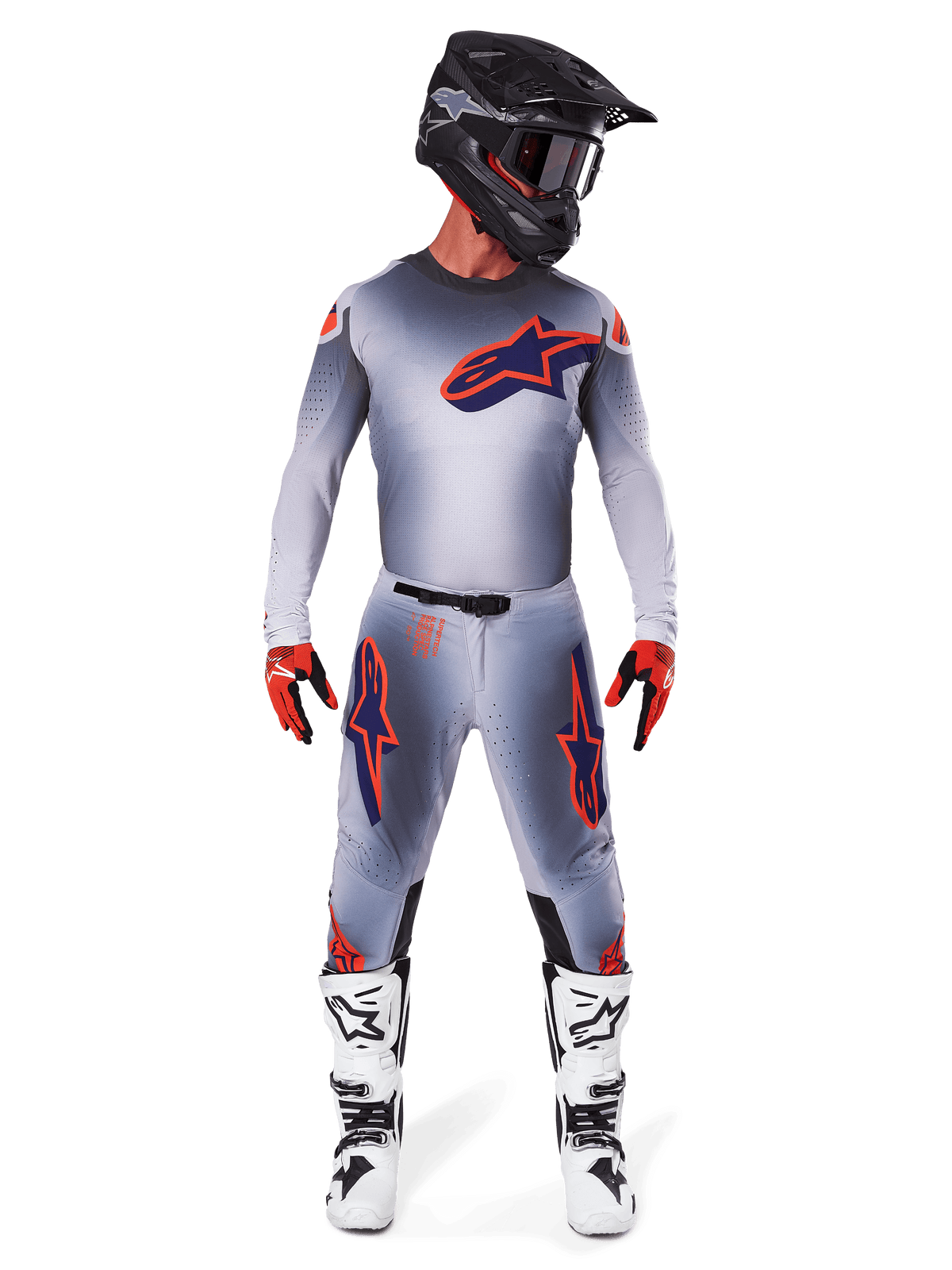 Piloto de motocross com calças Alpinestars 2025 Supertech Lipan e camisola a condizer em Cinza Laranja Fluo, com logótipos destacados em laranja e azul-escuro, combinado com capacete preto, luvas vermelhas e botas brancas e pretas, kit de corrida completo para performance todo-o-terreno