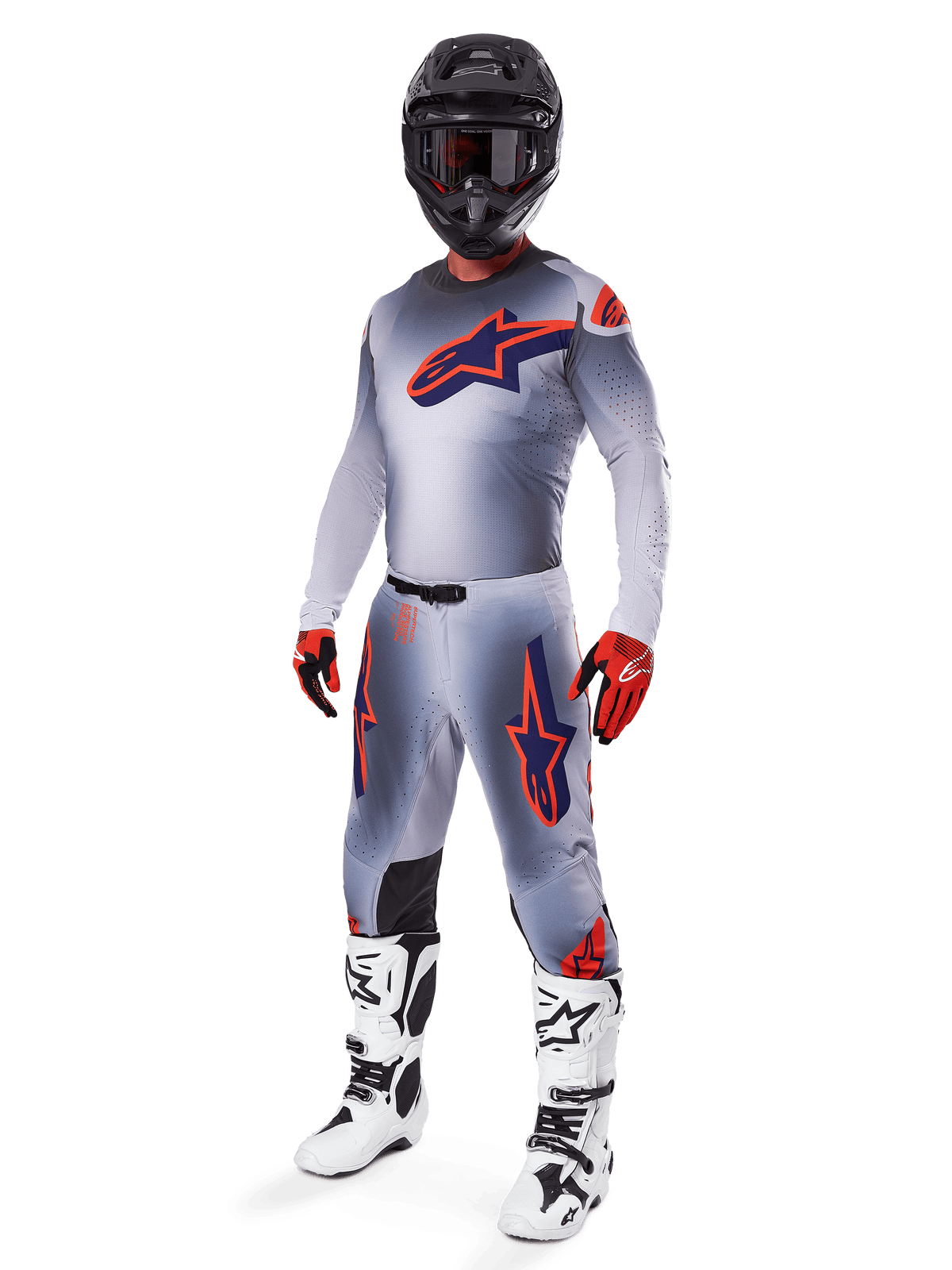 Piloto de motocross a usar o conjunto completo de equipamento de corrida Alpinestars 2025 Supertech Lipan, cinzento e laranja fluo, camisola cinzenta com logótipo laranja grande no peito, calças a condizer com detalhes em laranja, capacete preto, luvas vermelhas e botas brancas, fato de competição profissional todo-o-terreno