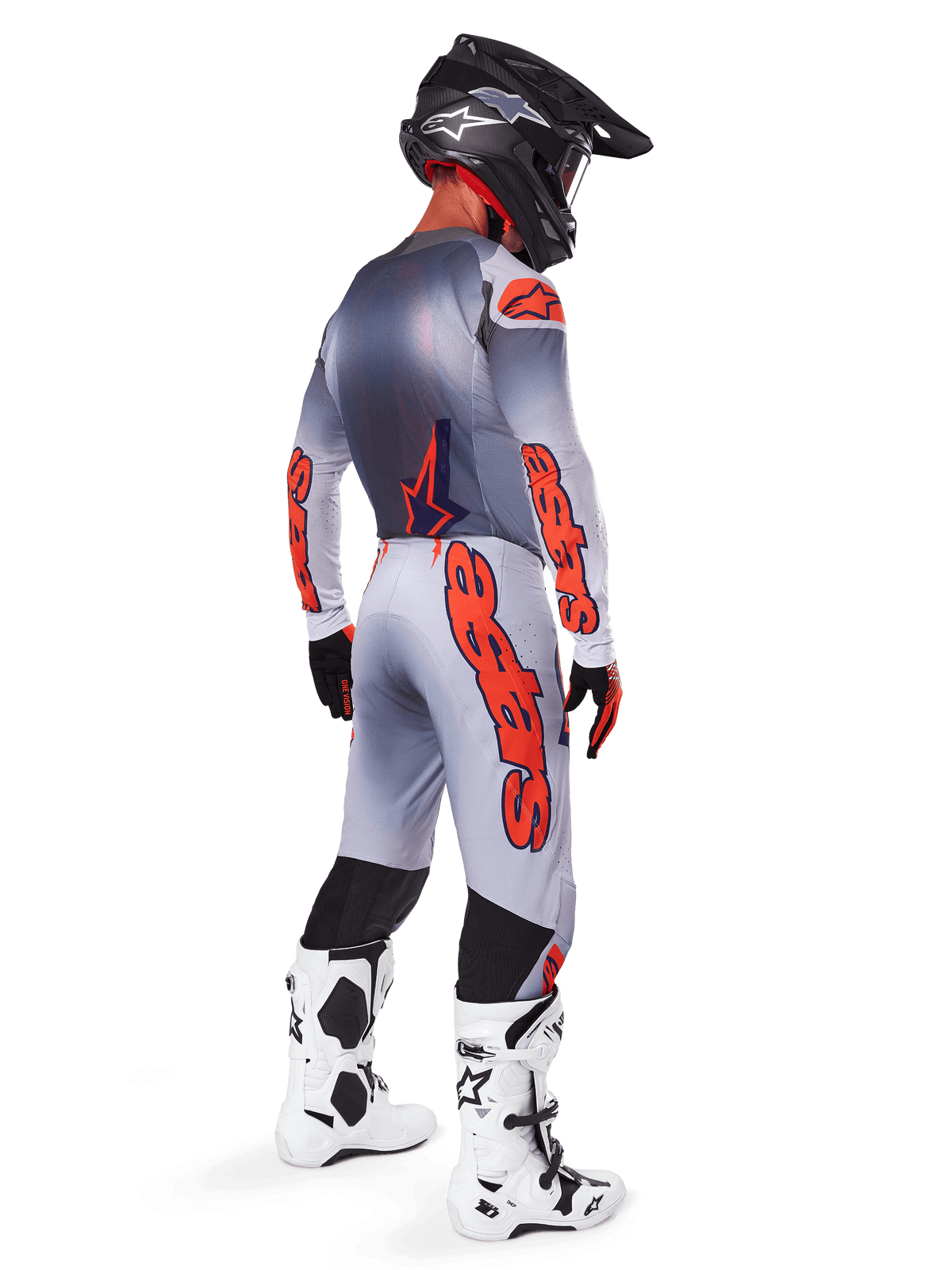 Piloto de motocross visto de costas a usar calças Alpinestars 2025 Supertech Lipan em cinzento e laranja fluo, camisola de manga comprida a condizer, capacete preto e botas técnicas brancas e pretas, equipamento profissional completo para todo-o-terreno.