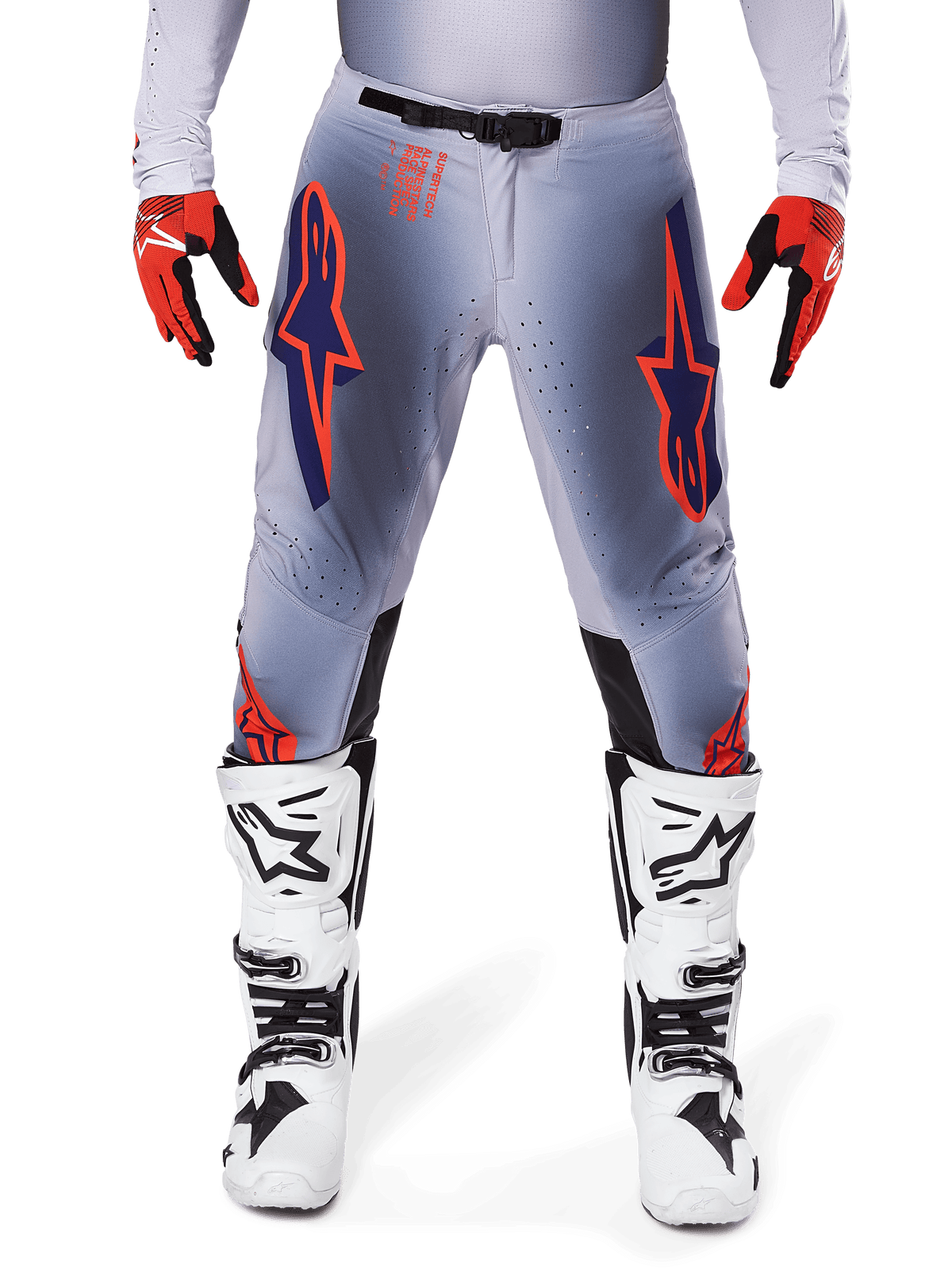 Alpinestars 2025 Supertech Lipan Pants, calças de motocross, cinzentas e laranja fluo, usadas com luvas vermelhas e pretas e botas brancas e pretas, com grandes logótipos de estrela Alpinestars nas coxas e perfurações de ventilação para competição de nível profissional.