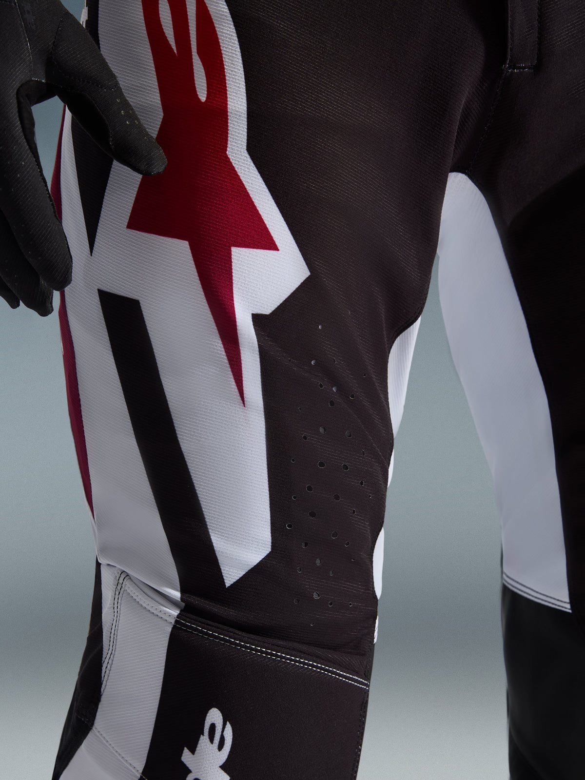 Alpinestars 2026 Supertech AFD Vista Pants, Motocross Pants, Black Red and White, close-up view of the thigh featuring a large red and white Astars logo and laser-cut perforations for ventilation.