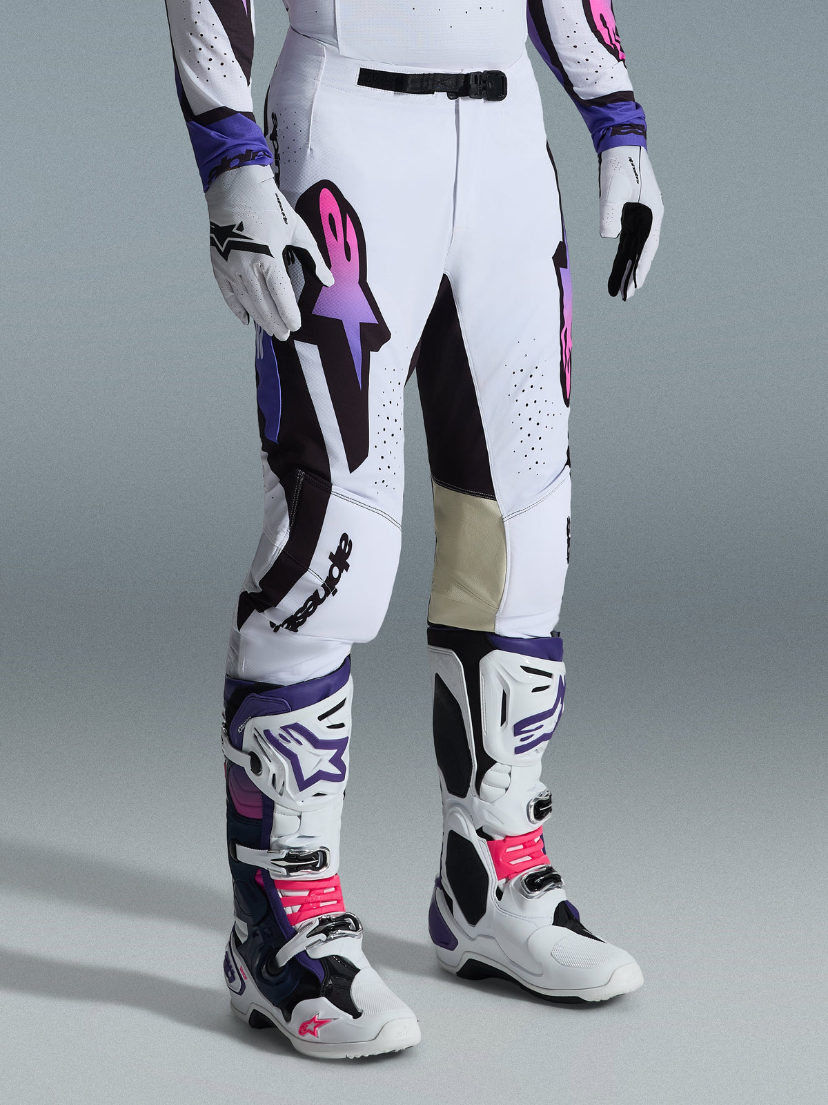 Alpinestars 2026 Supertech AFD Vista Pants, calças de motocross, brancas, roxas e pretas, com um logótipo Astar em degradê rosa e roxo, usadas com botas e luvas de motocross brancas e roxas a condizer, ajuste atlético de corrida com painéis internos nos joelhos em pele bege e detalhes perfurados.