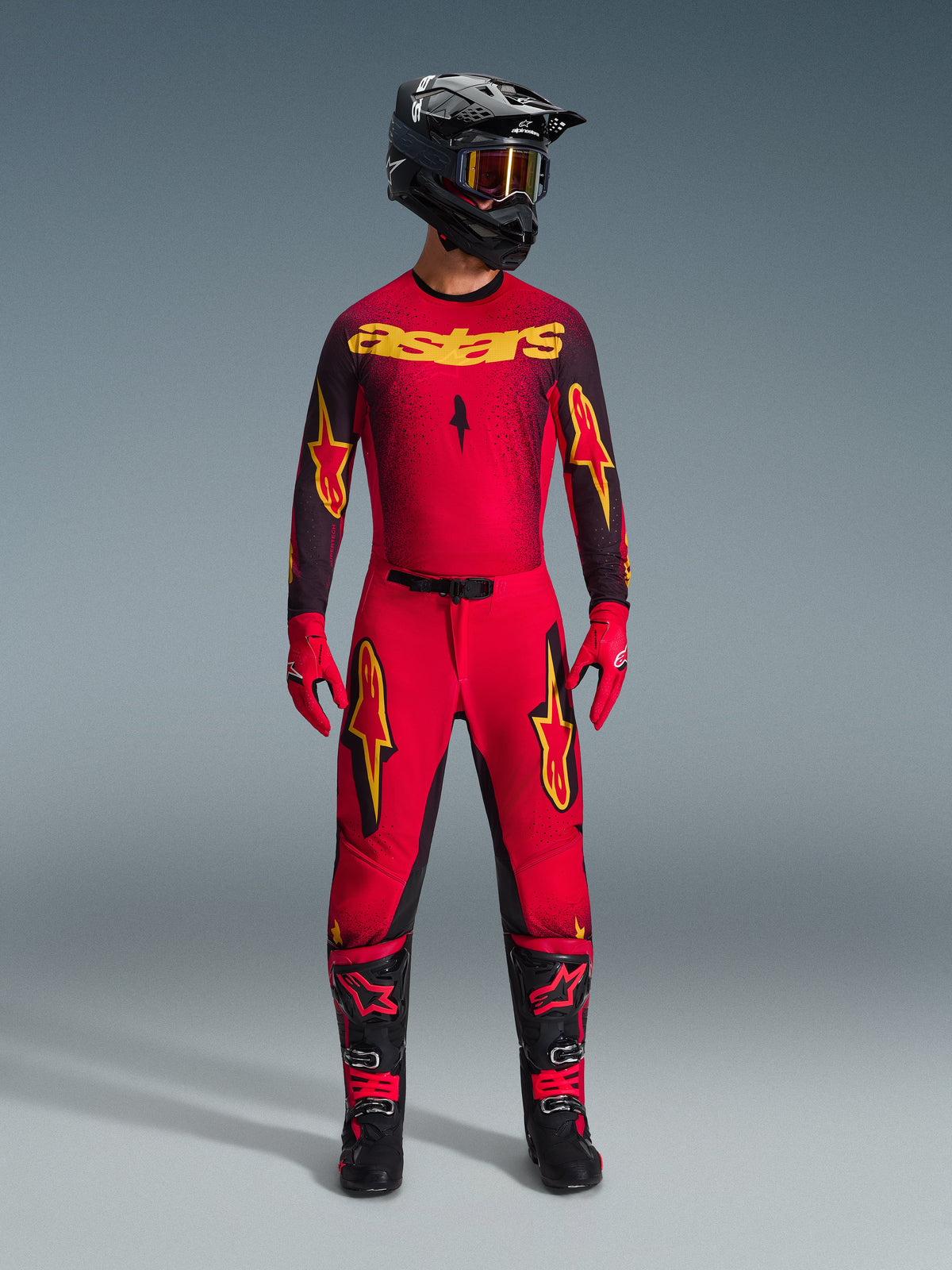 Calças Alpinestars 2026 Supertech Scenz, calças de motocross, vermelhas, pretas e amarelas, vestidas por um piloto num conjunto completo de competição, camisola vermelha e preta com logótipos amarelos, capacete preto, luvas vermelhas e botas pretas, design atlético pro-fit para competição todo-o-terreno