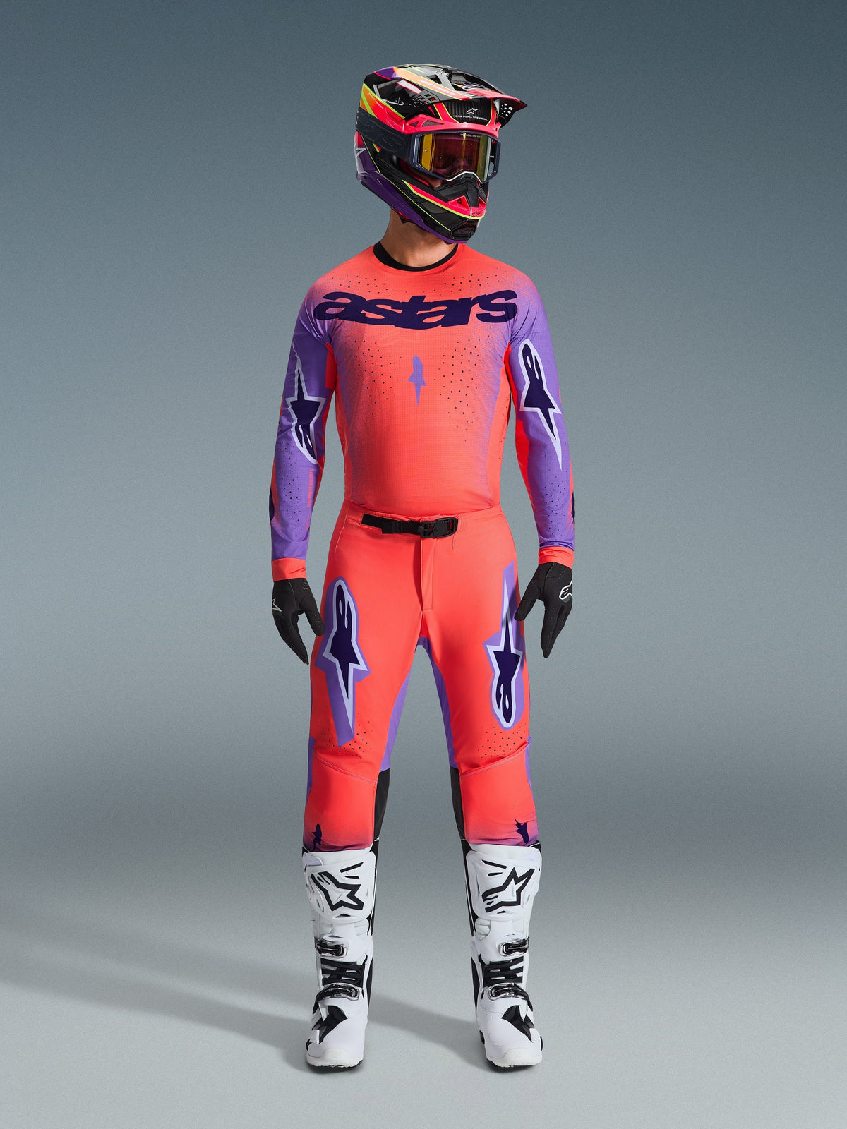Alpinestars 2026 Supertech Scenz Pants, calças de motocross, coral vibrante e roxo, usadas como um conjunto de equipamento completo com camisola e capacete a condizer, botas brancas e pretas, com logótipos roxos e ajuste atlético de corrida