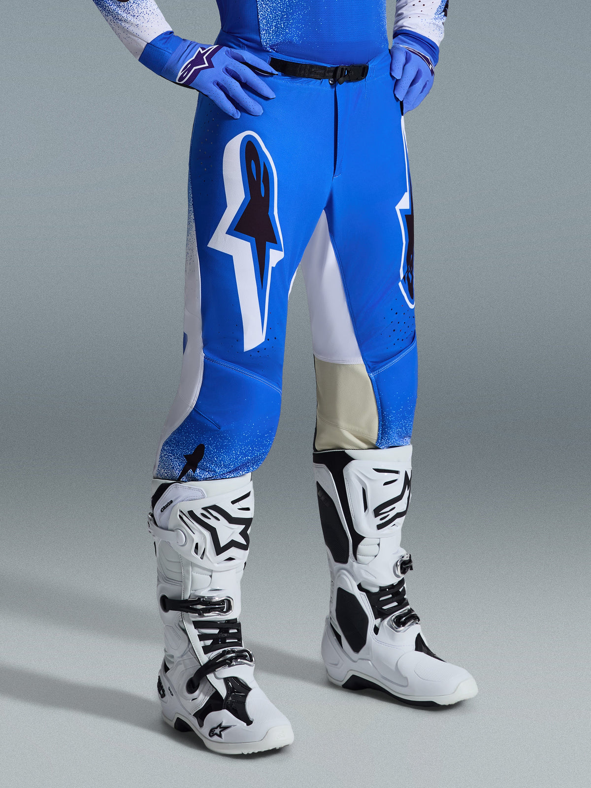 Alpinestars 2026 Supertech Scenz Pants, calças de motocross, azul UCLA e branco, usadas com botas brancas e pretas e luvas azuis, com grandes logótipos gráficos nas coxas e painéis brancos, ajuste atlético concebido para condução competitiva de motocross