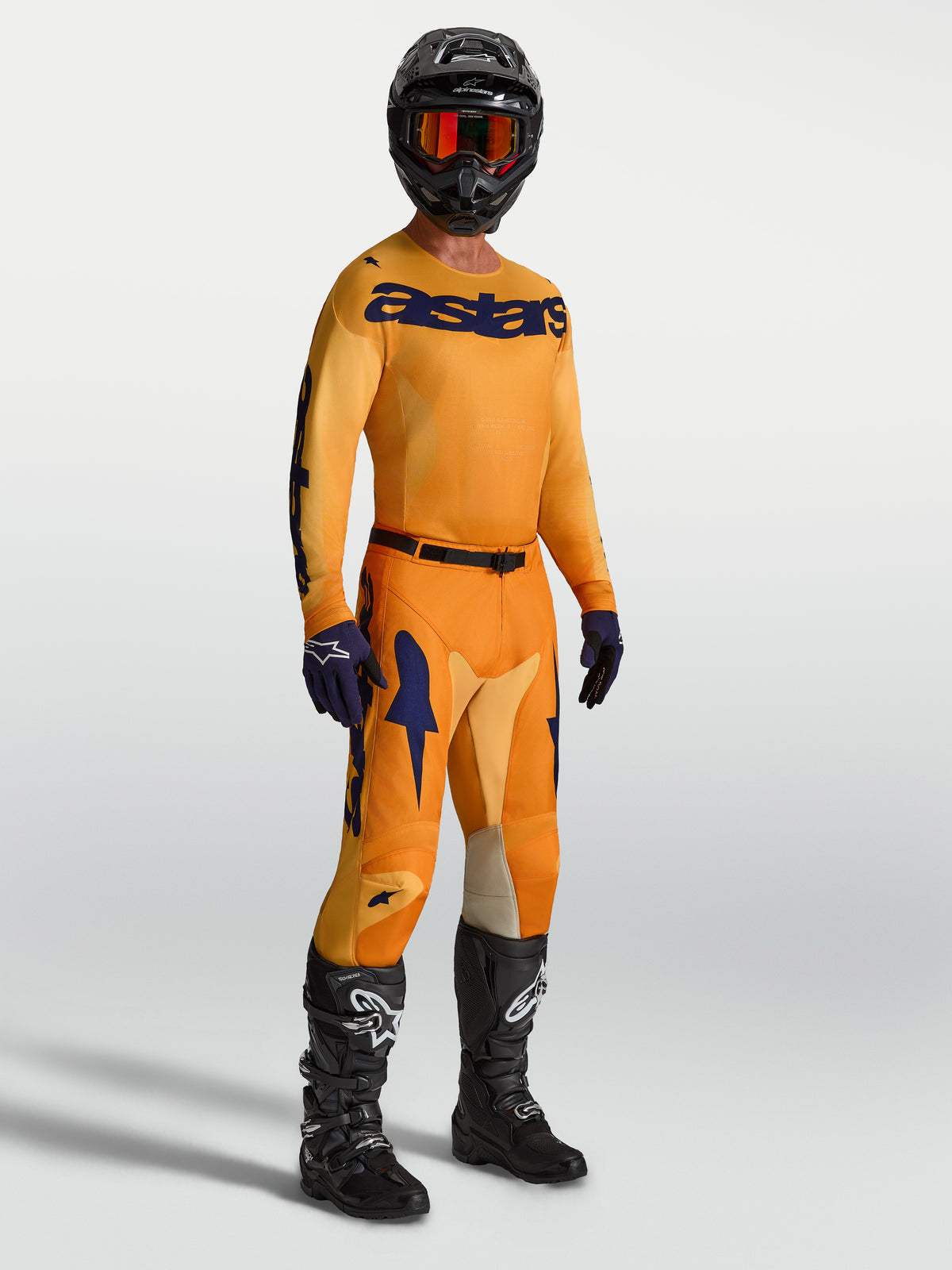 Alpinestars Calças e Camisola Racer Amber, equipamento de motocross para homem, laranja e azul escuro, com botas e capacete pretos.