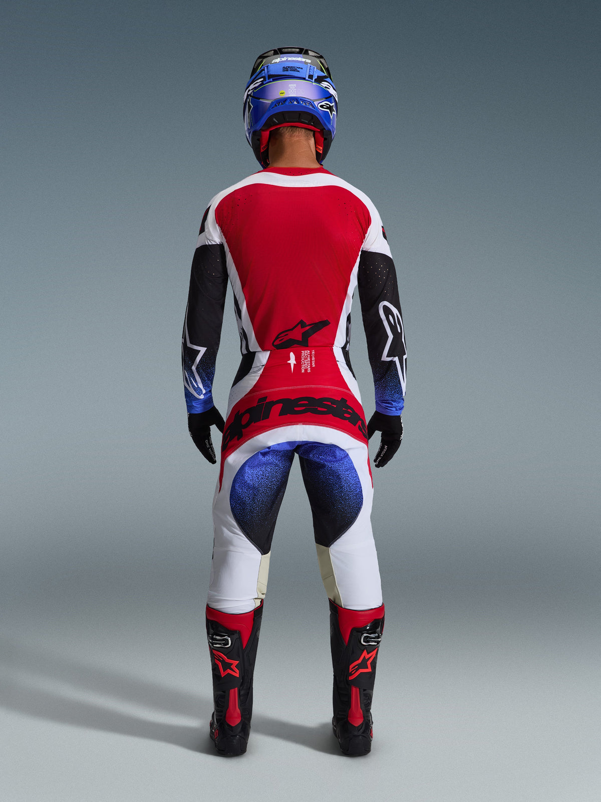 Alpinestars 2026 Techstar Knif Pants, Motocross Pants, Black White Red and Blue, back view of a rider in complete gear including matching jersey, blue helmet, and black and red boots, featuring bold Alpinestars branding on the seat.