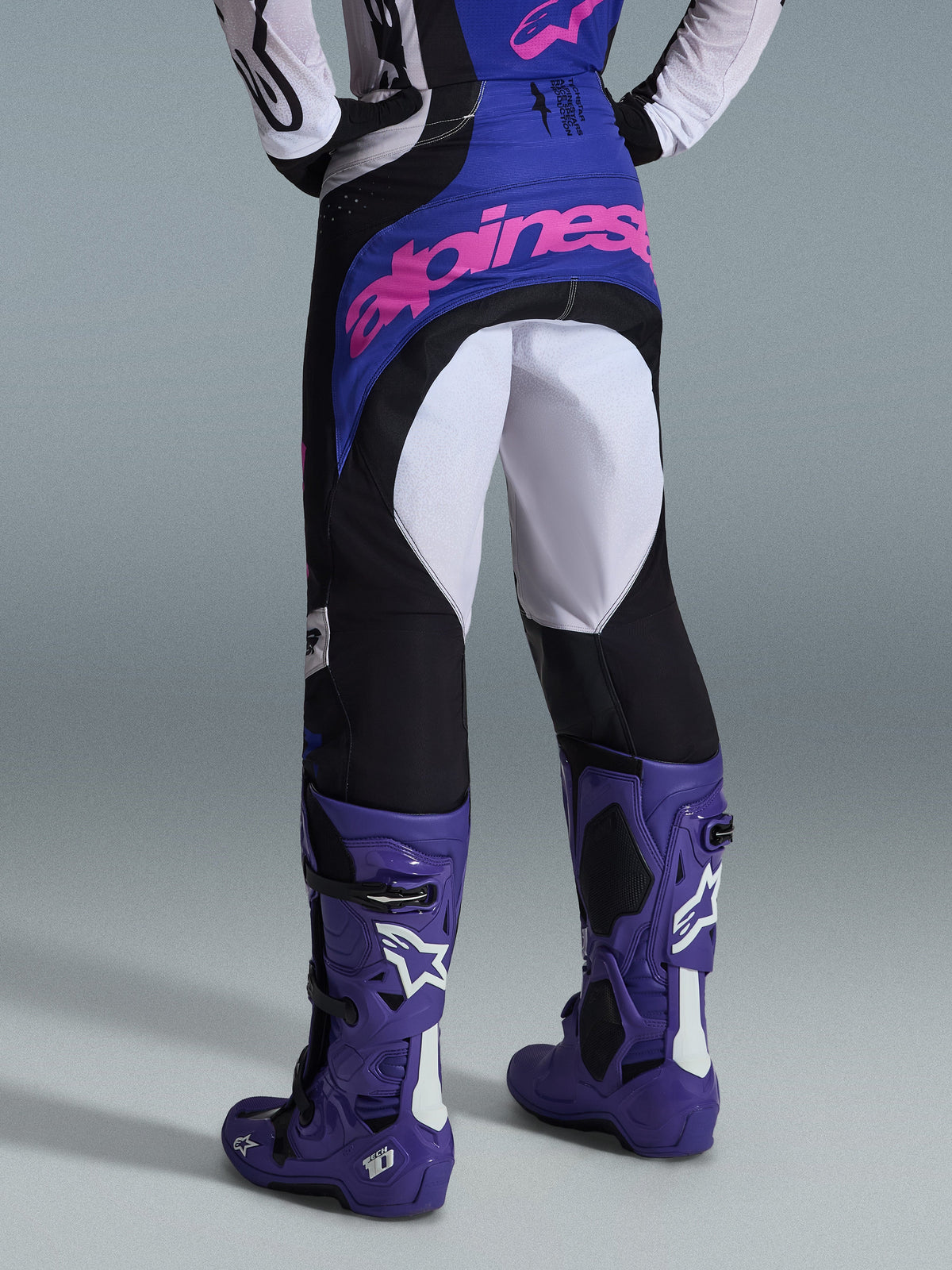 Alpinestars 2026 Techstar Knif Pants, calças de motocross, pretas, cinzento claro e roxo, vista traseira com logótipo rosa no assento, usadas com camisola a condizer e botas de motocross roxas, equipamento profissional de corrida todo-o-terreno