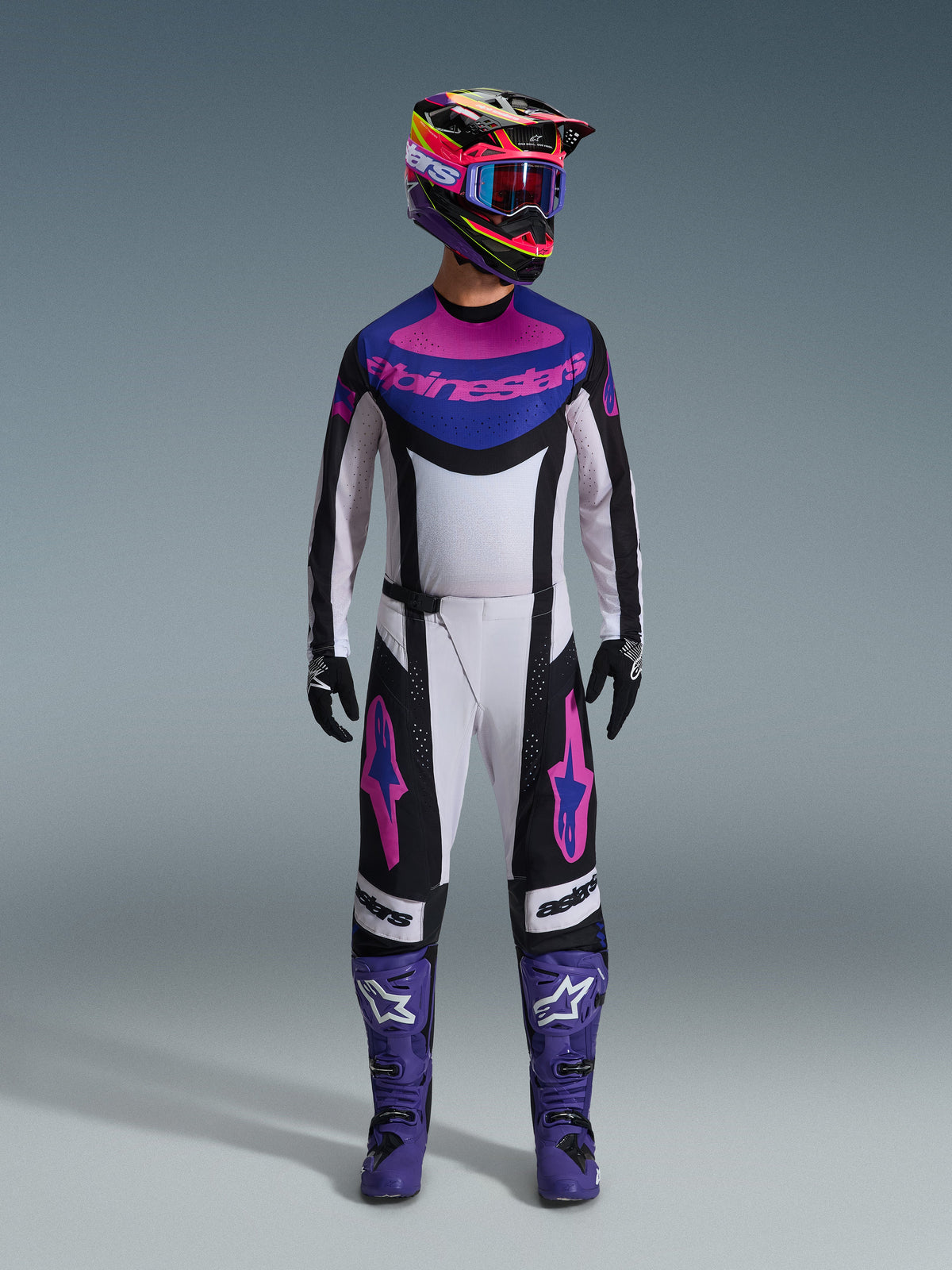 Alpinestars 2026 Techstar Knif Gear Set, equipamento completo de motocross, branco, preto, roxo e rosa, usado com um capacete multicolorido, óculos azuis, botas roxas e luvas pretas, conjunto de alta performance coordenado para corridas de todo-o-terreno
