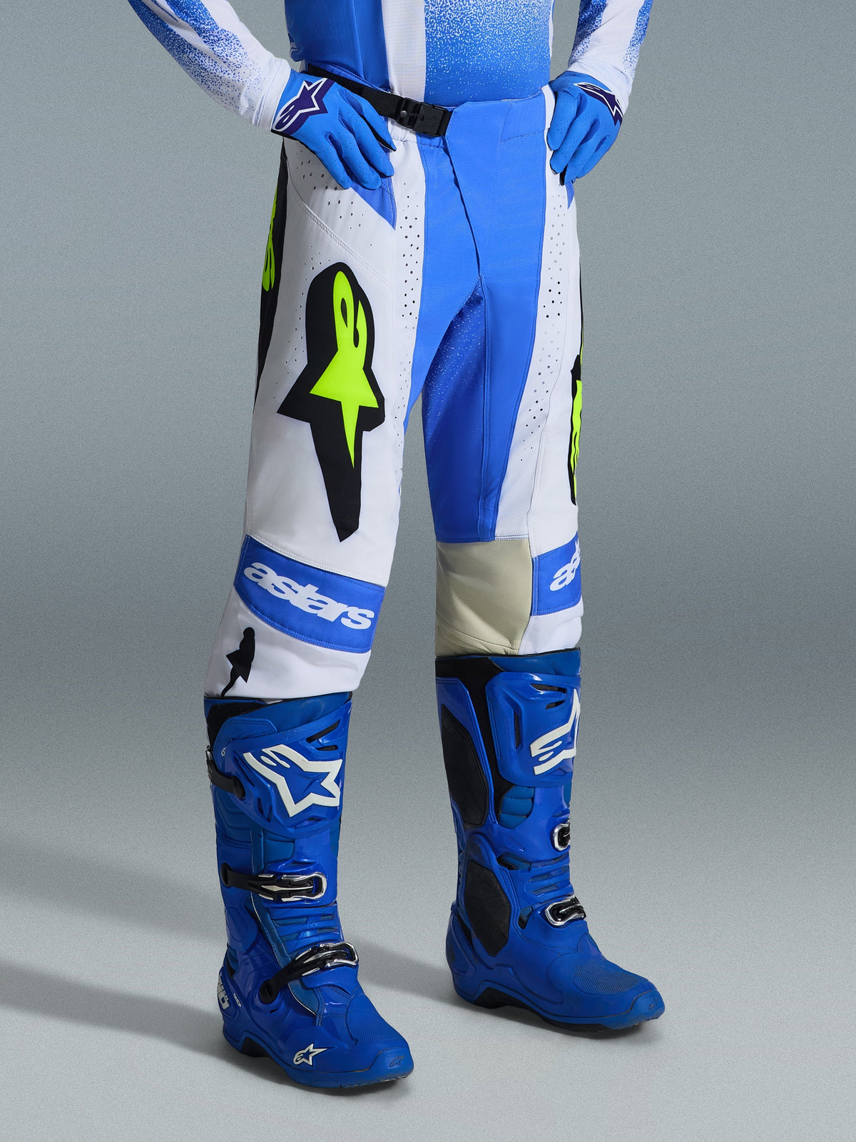 Alpinestars 2026 Techstar Knif Pants, calças de motocross, azul Ucla, branco e preto com amarelo néon, usadas com botas e luvas azuis a combinar, com logótipos Alpinestars e Astar em destaque, equipamento de alto desempenho para todo-o-terreno