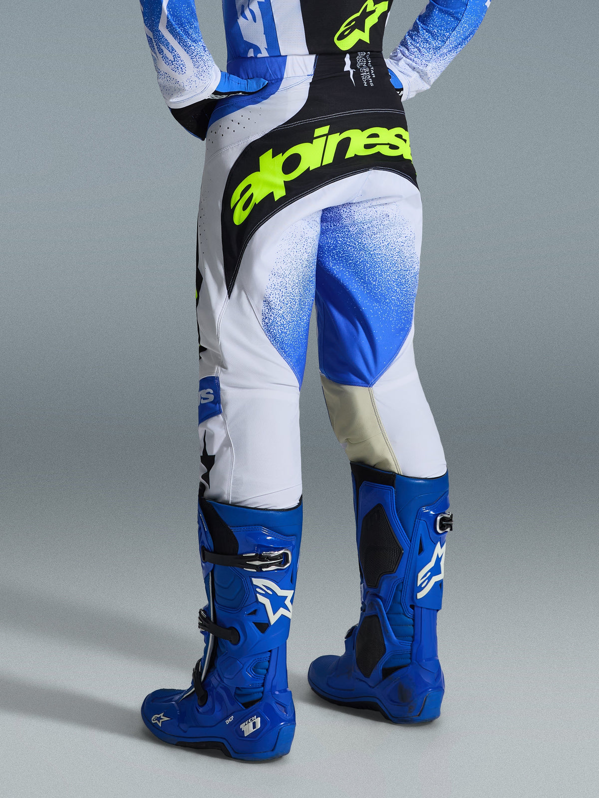Alpinestars 2026 Techstar Knif Pants, calças de motocross, azul Ucla, preto e amarelo fluo, vista traseira com painéis brancos e padrão degradê azul em spray, logótipo amarelo fluo no assento preto, usadas com botas Tech 10 e camisola azuis para corridas todo-o-terreno