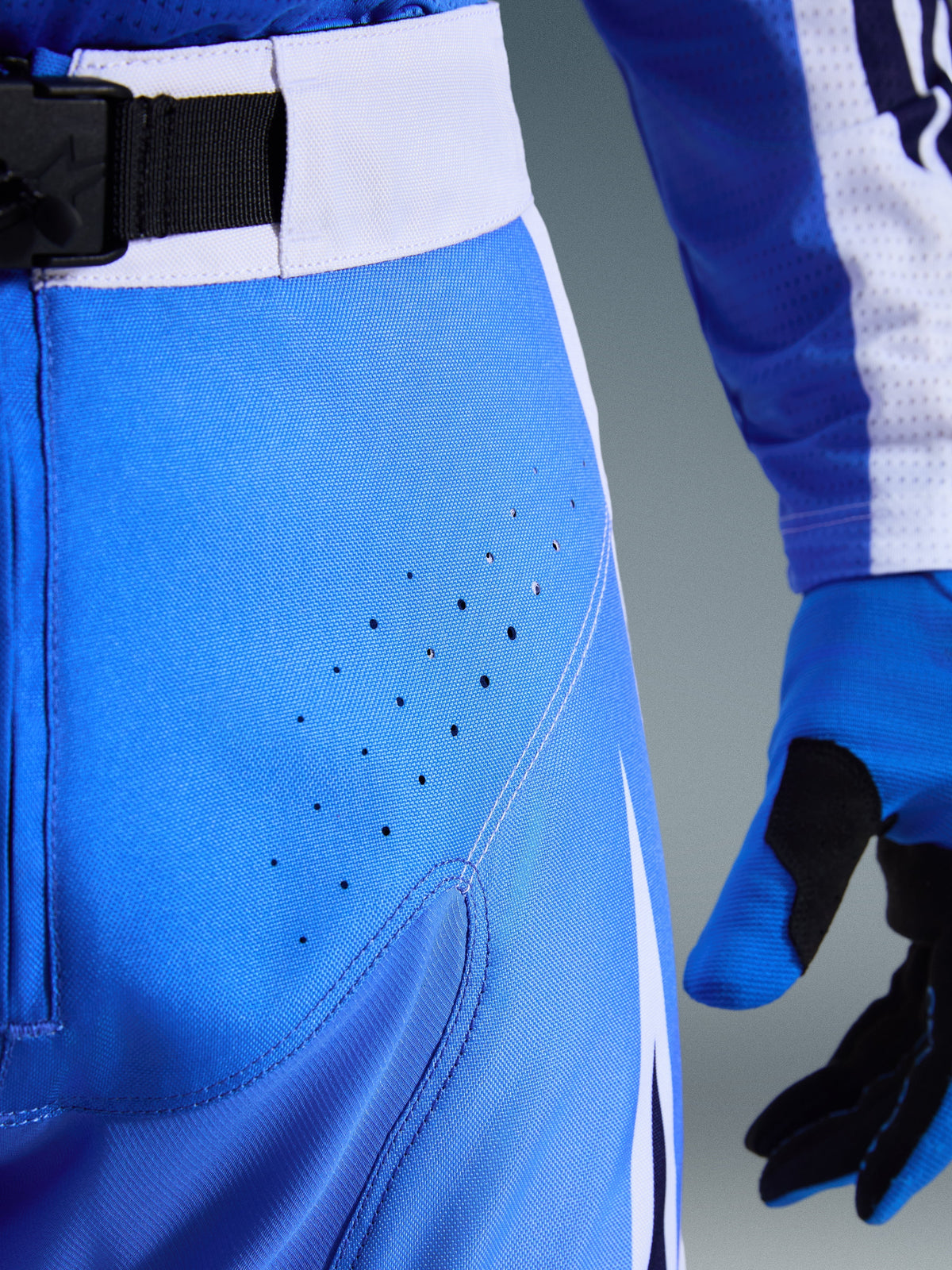 Calças Alpinestars Techstar Knif 2026, calças de motocross, azul UCLA e preto, vista de pormenor da coxa com perfurações cortadas a laser e fivela magnética SX2 na cintura, construção técnica para competições todo-o-terreno