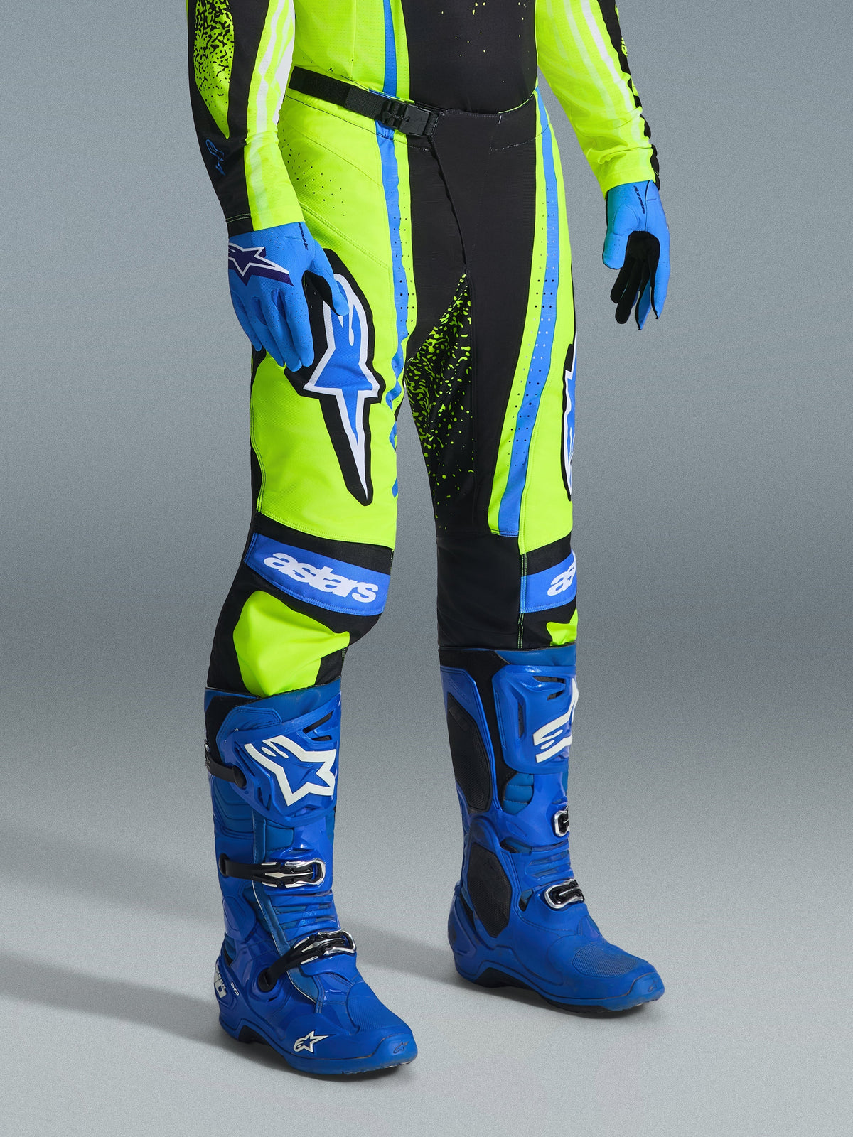 Alpinestars 2026 Techstar Nomur Pants, calças de motocross, amarelo néon, azul-marinho e azul UCLA, usadas com botas e luvas azuis a condizer, com logótipos brancos destacados e painéis reforçados, equipamento profissional de corrida todo-o-terreno