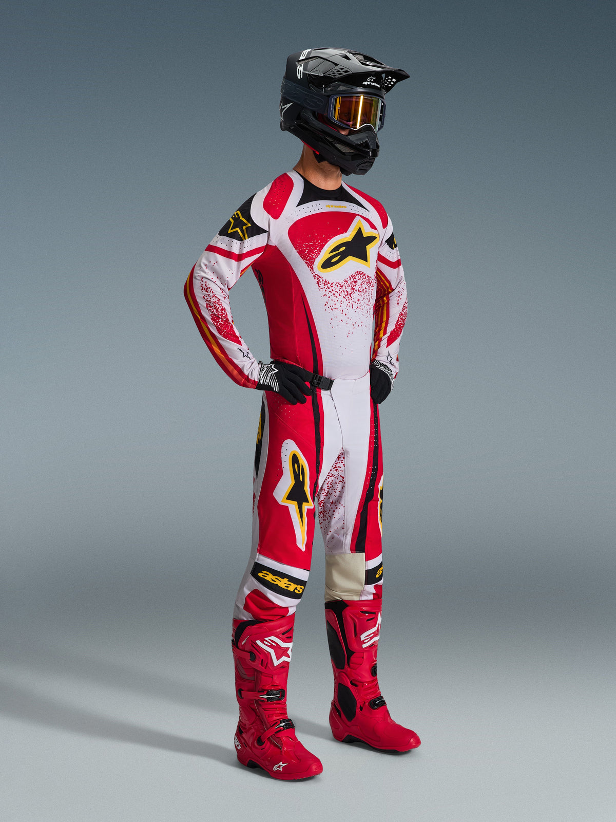 Piloto de motocross com o Conjunto de Equipamento Alpinestars Techstar Nomur 2026, vermelho e branco com detalhes pretos e logótipos amarelos, botas vermelhas a combinar e capacete preto, fato de corrida profissional para competição de todo-o-terreno