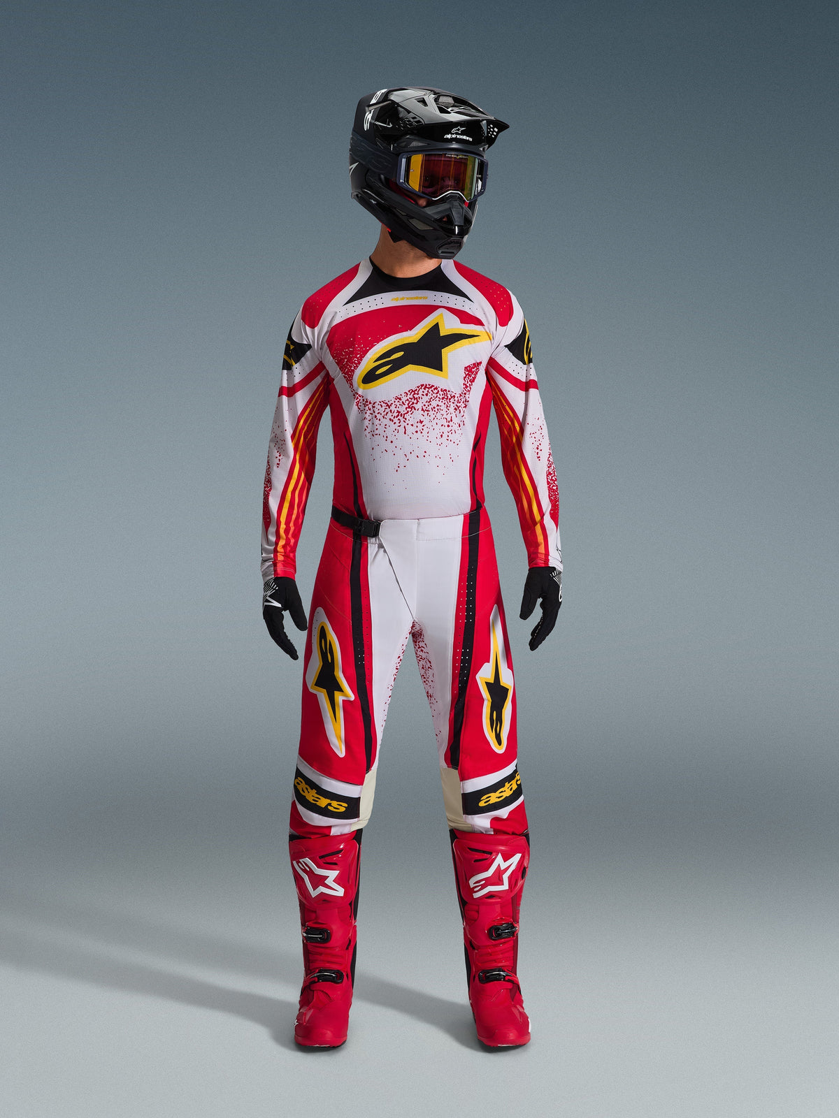 Camisola Alpinestars Techstar Nomur 2026, vermelha e branca com detalhes em preto e logótipos amarelos, usada por um piloto de motocross com calças a condizer, botas vermelhas e um capacete preto, equipamento de corrida profissional para todo-o-terreno