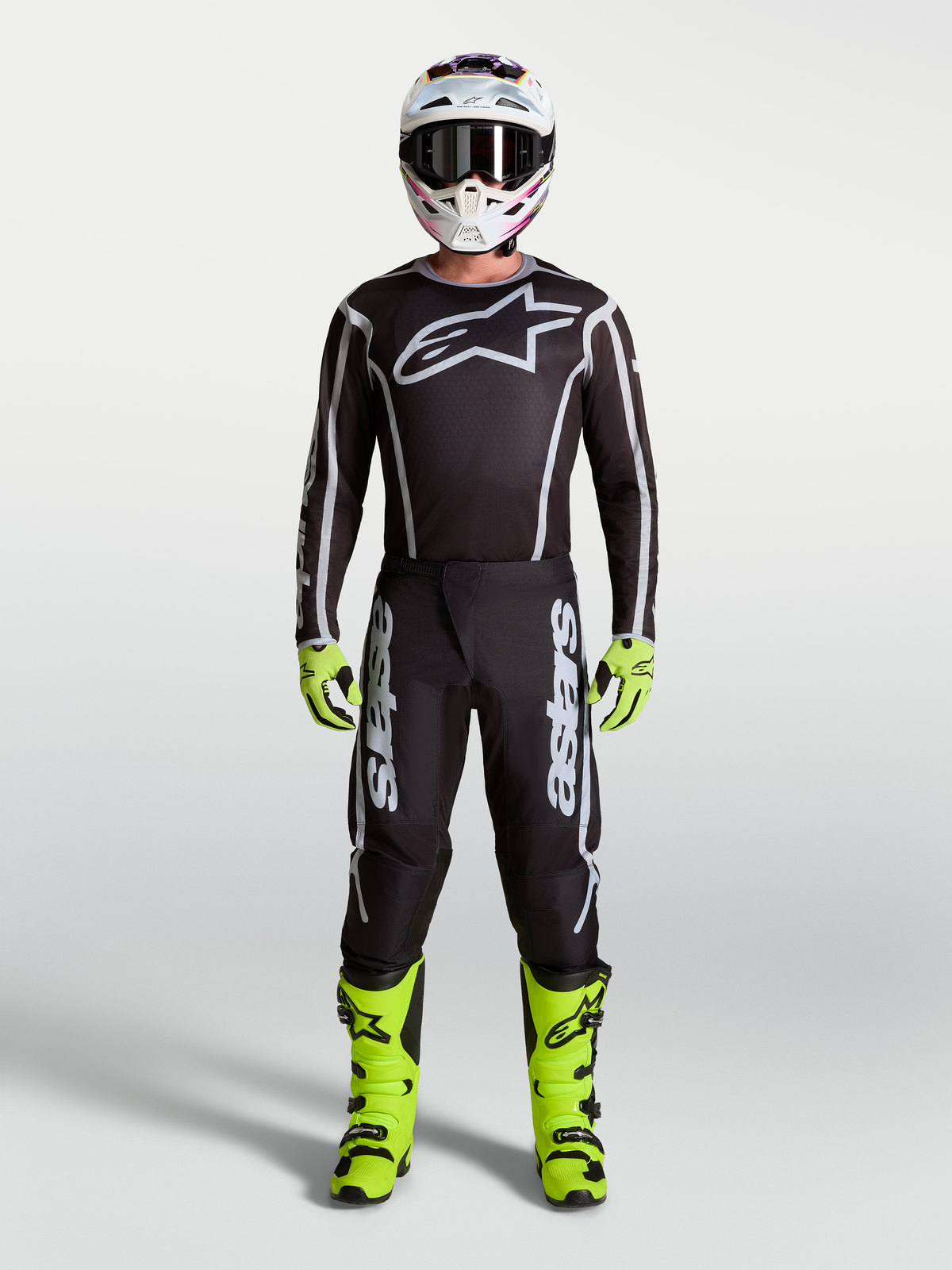 Alpinestars calças Fluid Apex V2, calças de motocross para homem, pretas e prateadas, com botas néon, camisola e capacete.