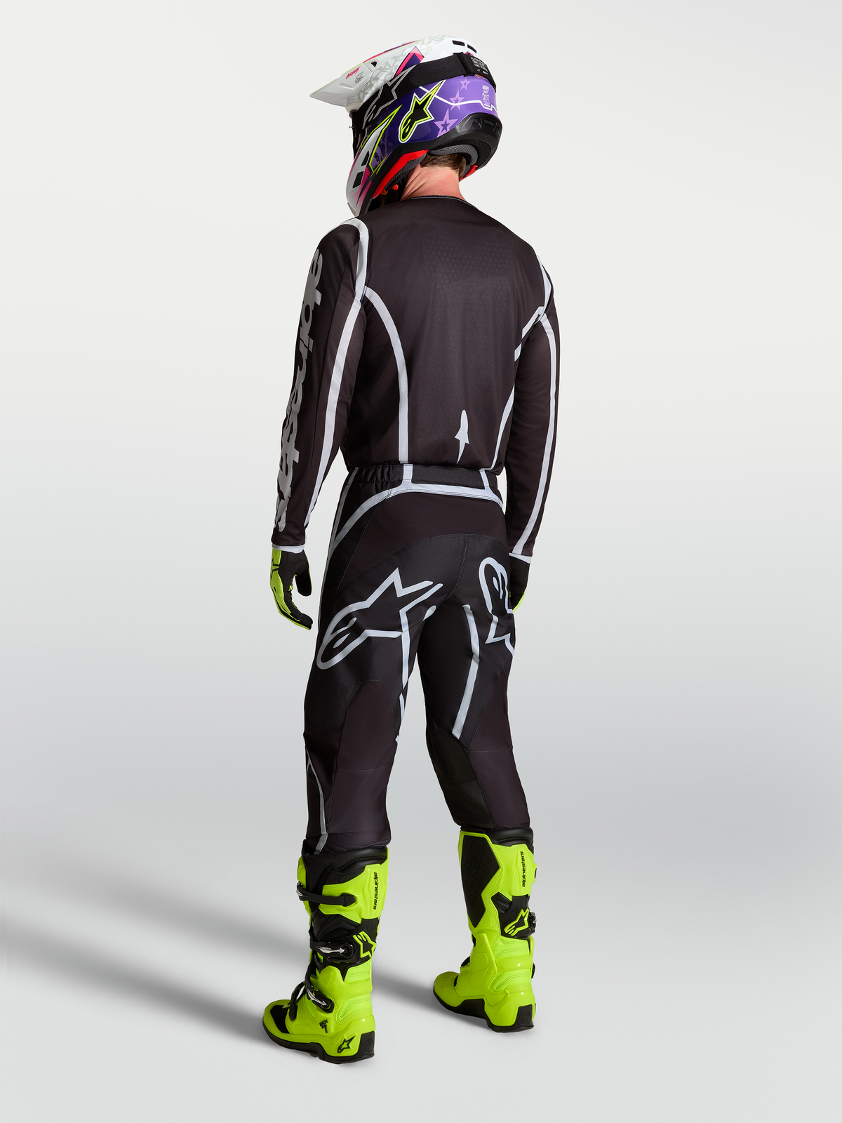 Alpinestars calças Fluid Apex V2 de homem, calças de motocross pretas e prateadas, vista traseira com camisola e botas néon.