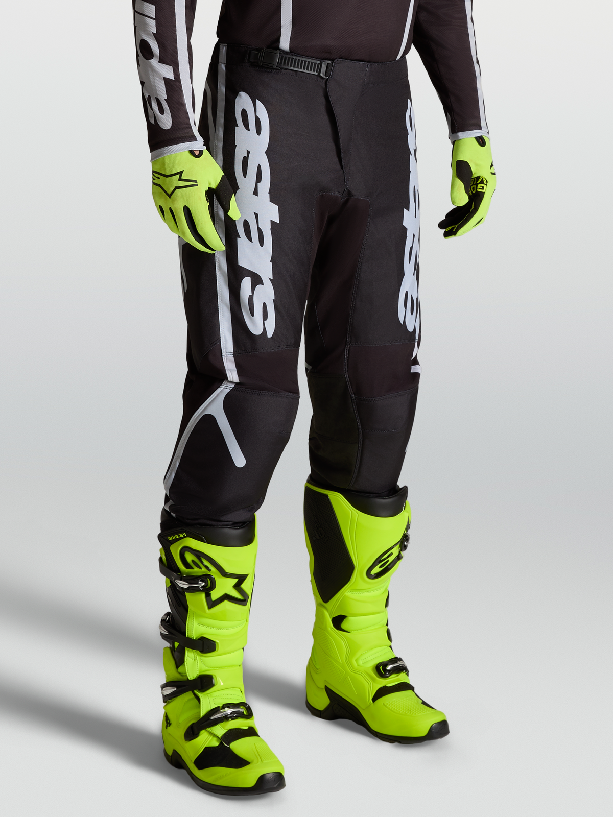 Calças Alpinestars Fluid Apex V2, equipamento de motocross para homem, pretas e prateadas, com botas amarelas vibrantes.