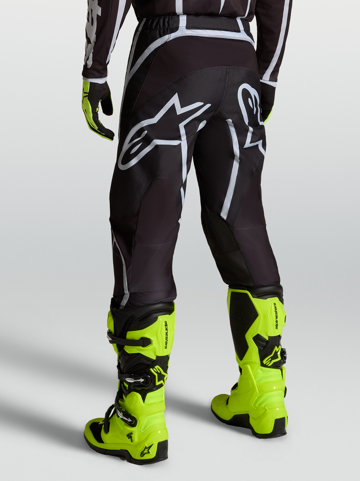 Alpinestars Calças Fluid Apex V2, calças de motocross para homem, preto e prateado, vista traseira e botas amarelo-fluorescentes