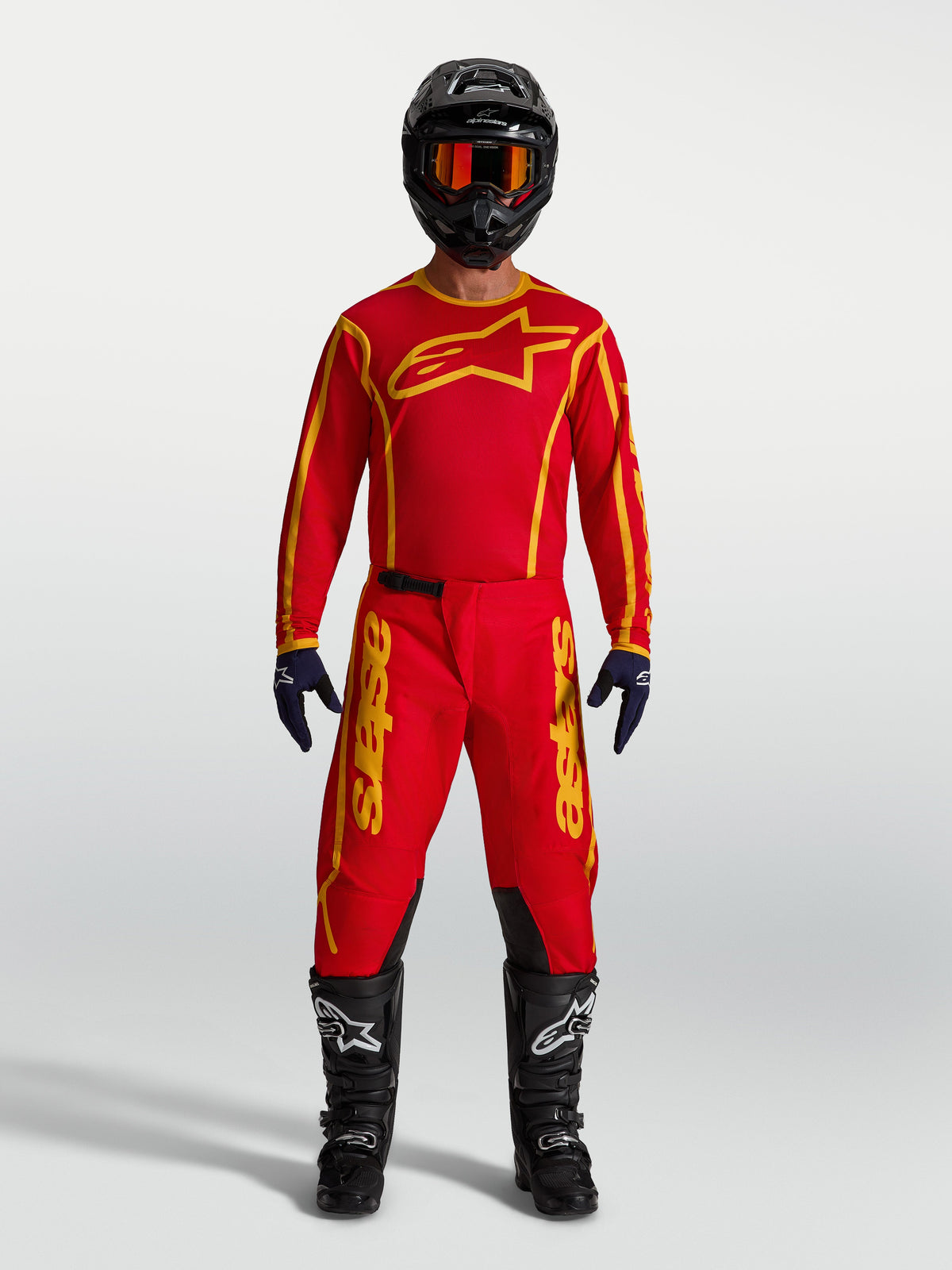 Alpinestars Fluid Apex V2, calças de motocross para homem, vermelho e dourado, com camisola, capacete e botas pretas.
