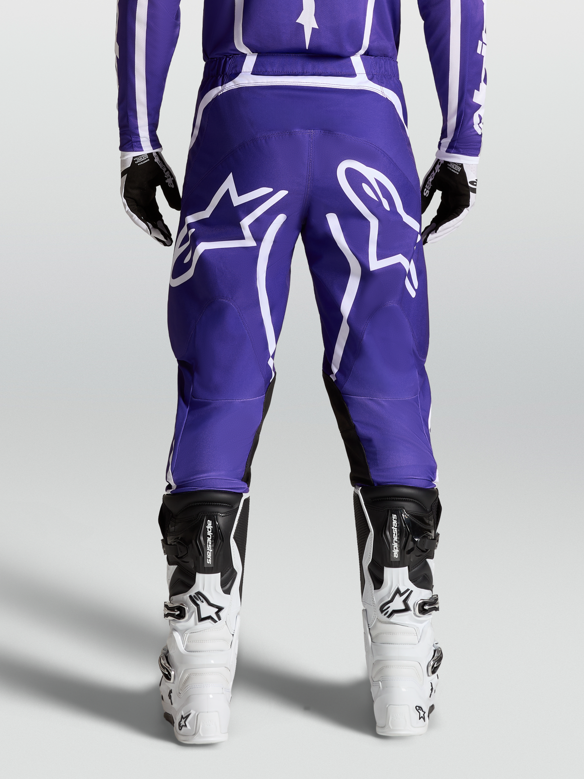 Alpinestars Calças Fluid Apex V2, calças de motocross para homem, azuis e brancas, construção robusta 600D, vista traseira no modelo com botas.
