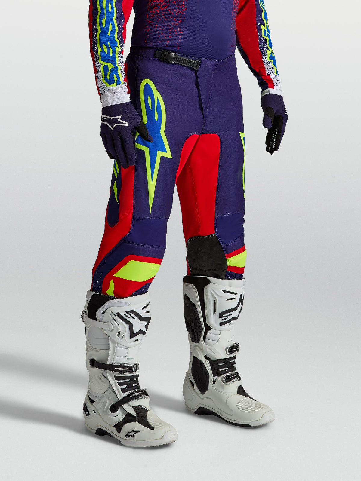 Calças Alpinestars Fluid Drag, calças de motocross para homem, azul-marinho e vermelhas, gráficos vibrantes e botas brancas.
