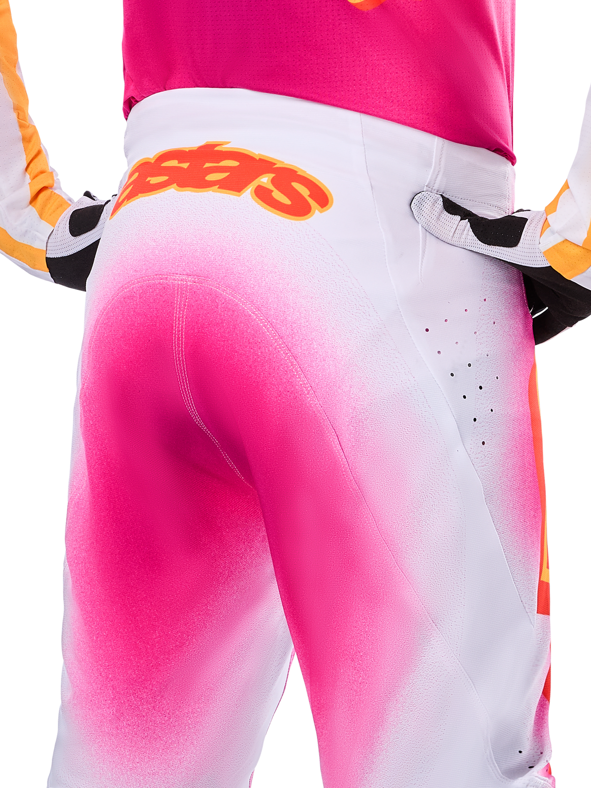 Alpinestars Calças Supertech AFD MIG Edição Limitada, calças de motocross, rosa fluo e branco com efeito degradê de tinta em spray, grande logótipo Alpinestars cor de laranja no cós traseiro, vista em grande plano do ajuste atlético e perfurações de ventilação