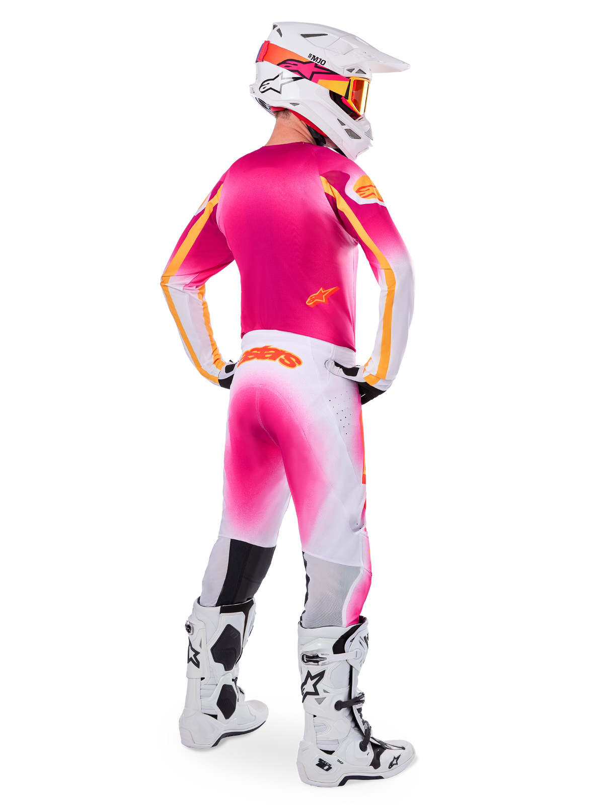 Piloto de motocross visto de costas a usar o conjunto de equipamento Limited Edition Supertech AFD MIG, camisola cor-de-rosa com detalhes cor de laranja, calças brancas com degradê cor-de-rosa e marca Alpinestars em cor de laranja, capacete branco com grafismos cor-de-rosa e óculos cor de laranja, botas brancas e pretas, kit de competição profissional para todo-o-terreno