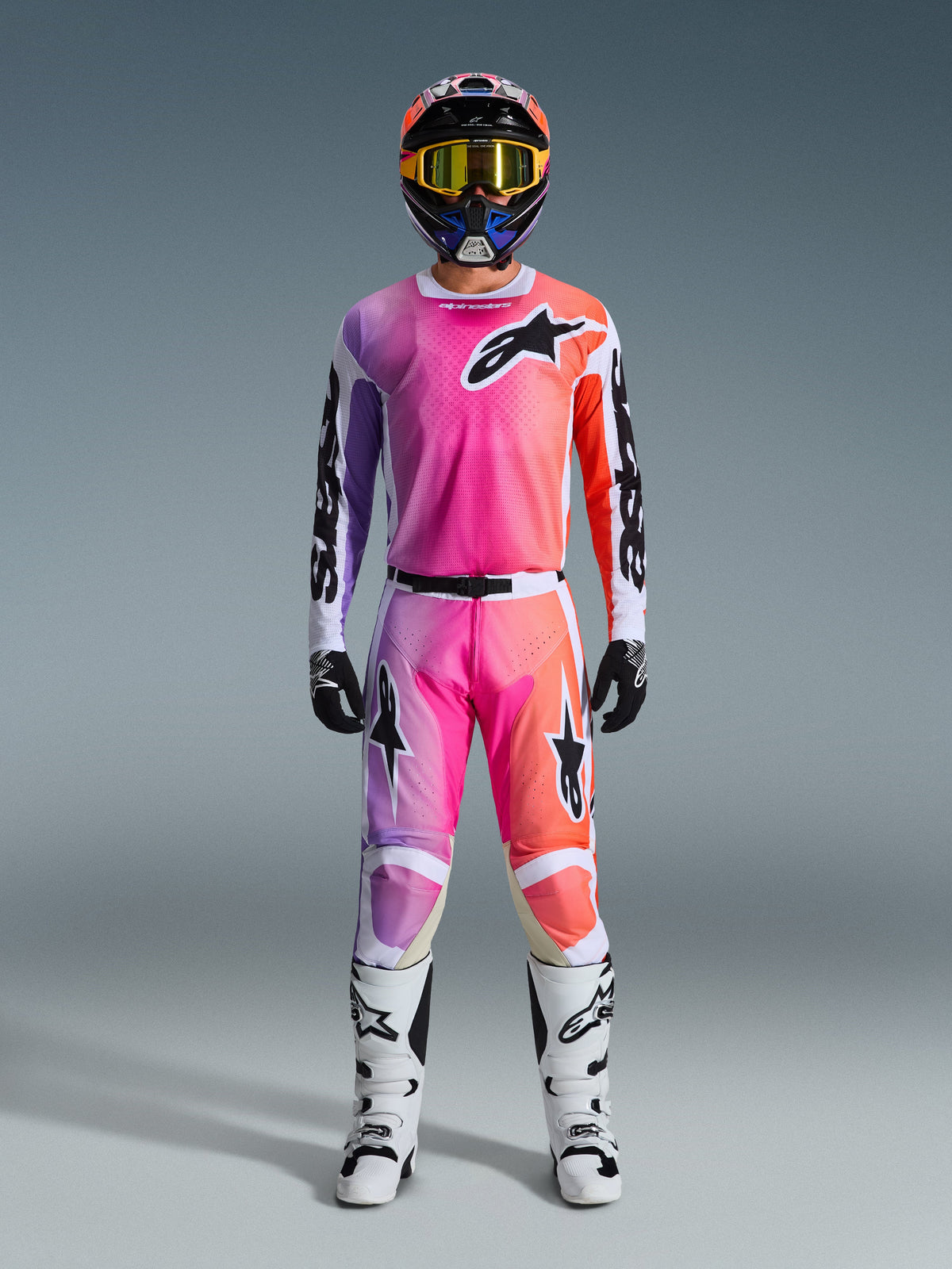 Motocross rider wearing the 2026 Racer Air Portl Jersey and matching pants, featuring a pink, purple, and orange gradient with black Alpinestars logos, white racing boots, black gloves, and a multicolor helmet, professional off-road racing gear.
