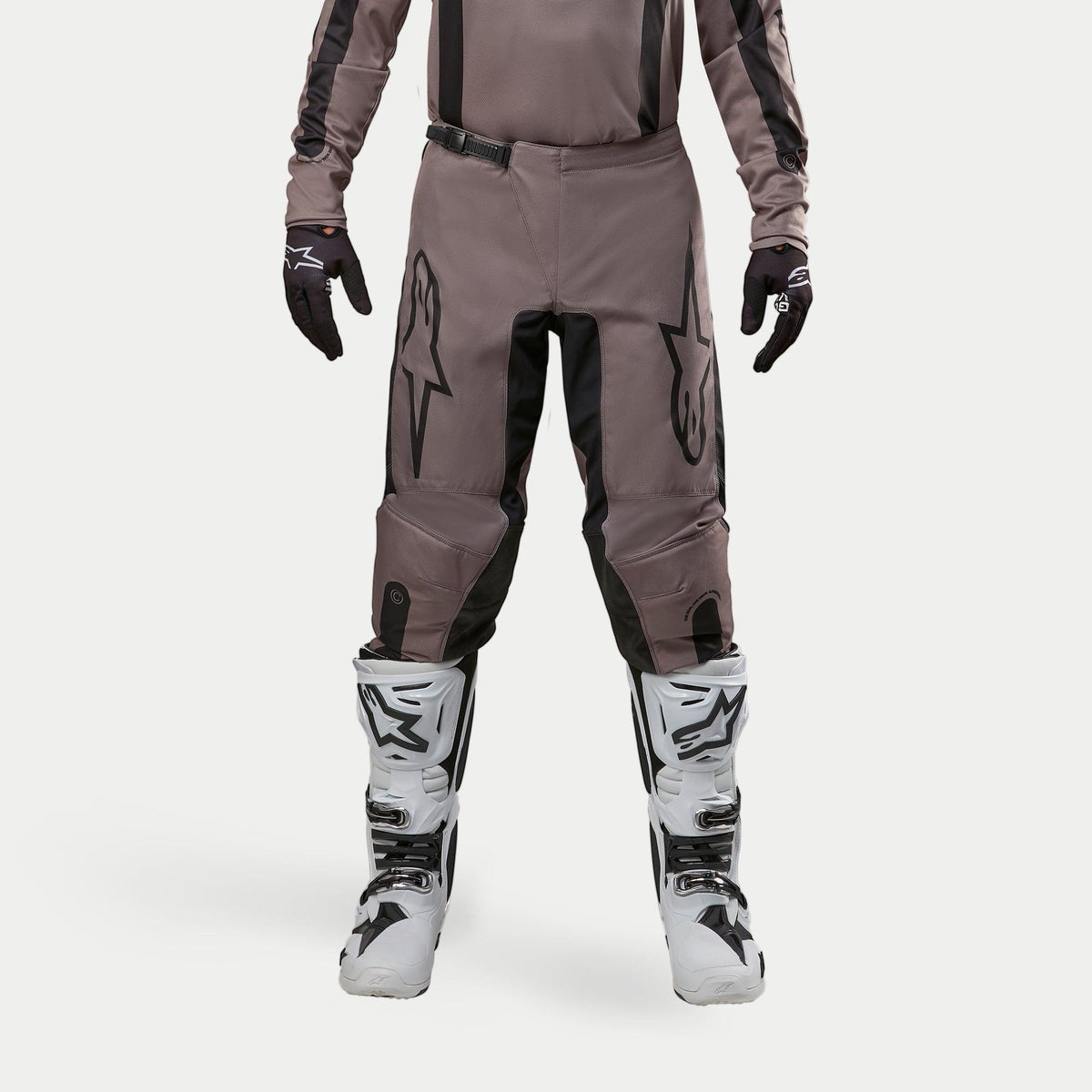 Calças Alpinestars 2024 Fluid Lurv, calças de motocross, Mud Black, usadas com camisola a condizer, luvas pretas e botas brancas, com grandes logótipos pretos nas coxas, ajuste ergonómico e material durável para competições todo-o-terreno