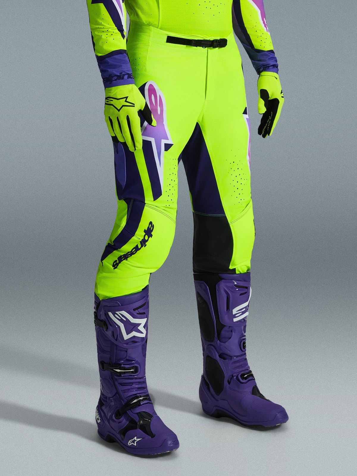 Alpinestars 2026 Supertech Vista Pants, calças de motocross, amarelo néon brilhante, roxo e preto, usadas com botas roxas e luvas amarelas a condizer, com logótipo em destaque na coxa e corte atlético de alta performance