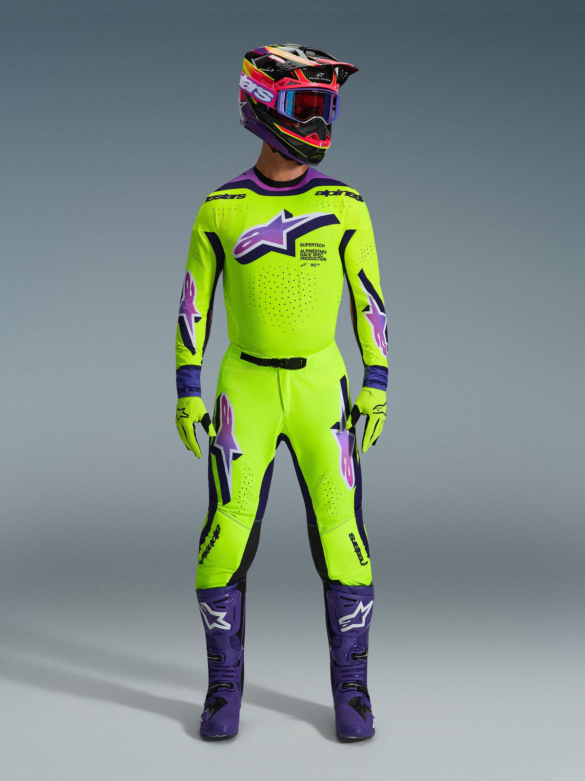 Alpinestars 2026 Supertech Vista Pants, calças de motocross, amarelo néon com detalhes roxos e pretos, usadas como parte de um conjunto de equipamento de corrida coordenado com camisola, capacete e botas roxas a condizer, com um ajuste atlético profissional e logótipos arrojados para performance em todo-o-terreno