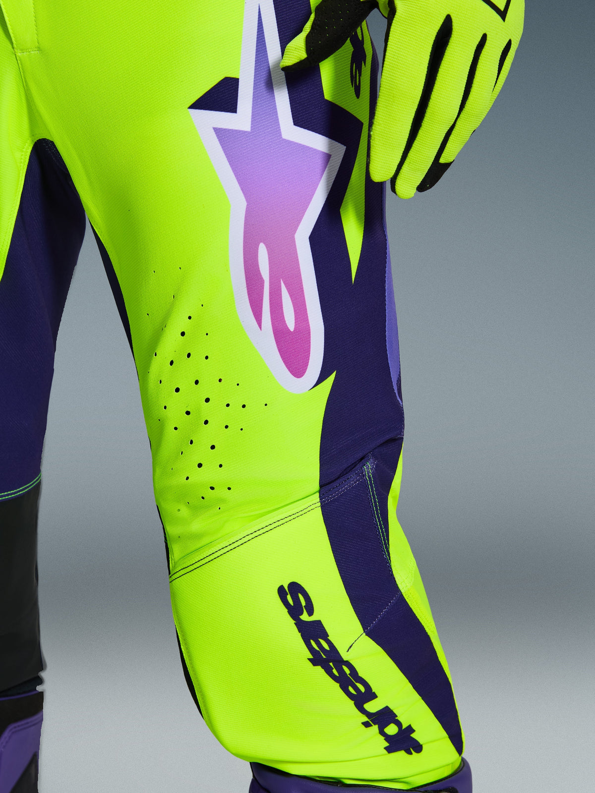Alpinestars 2026 Supertech Vista Pants, calças de motocross, amarelo, roxo e preto, detalhe do logótipo de estrela com gradiente e perfurações de ventilação cortadas a laser, combinadas com luvas de corrida a condizer