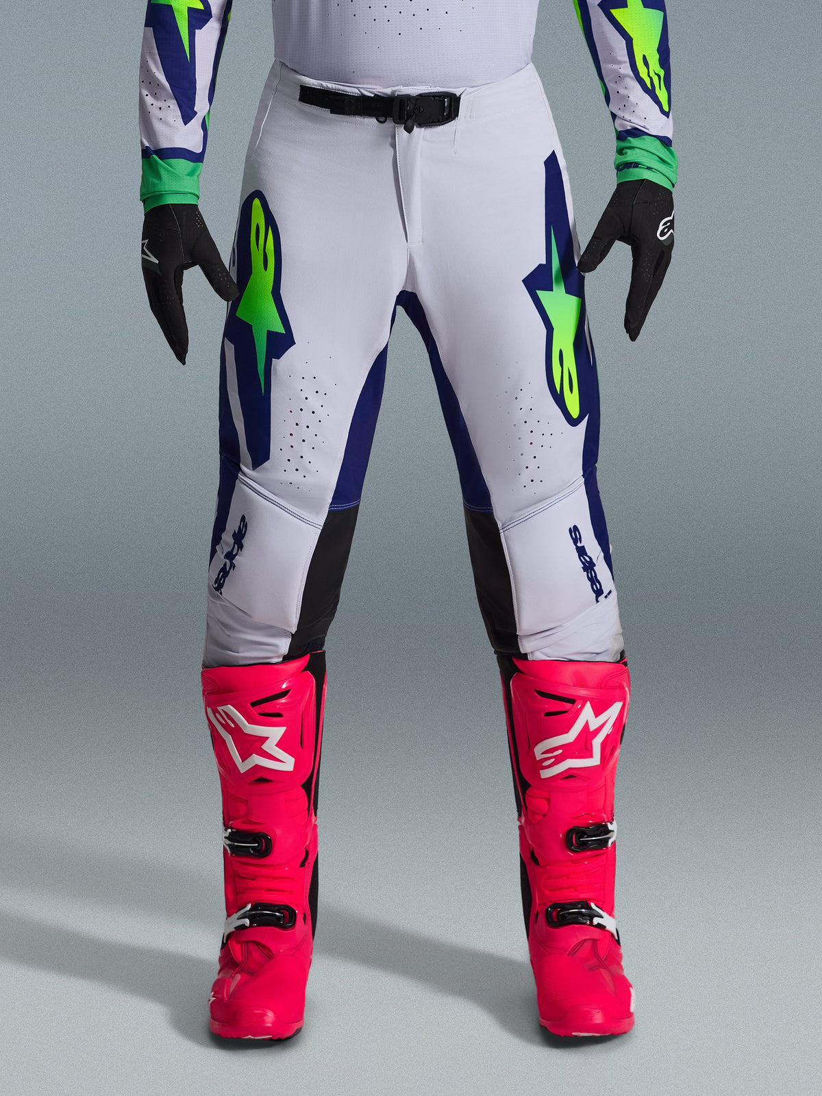 Conjunto de Equipamento Alpinestars 2026 Supertech Vista, calças de motocross em branco com detalhes em azul e verde lima, combinadas com botas cor-de-rosa vibrante e luvas pretas, equipamento de competição de nível profissional com corte atlético e perfurações a laser