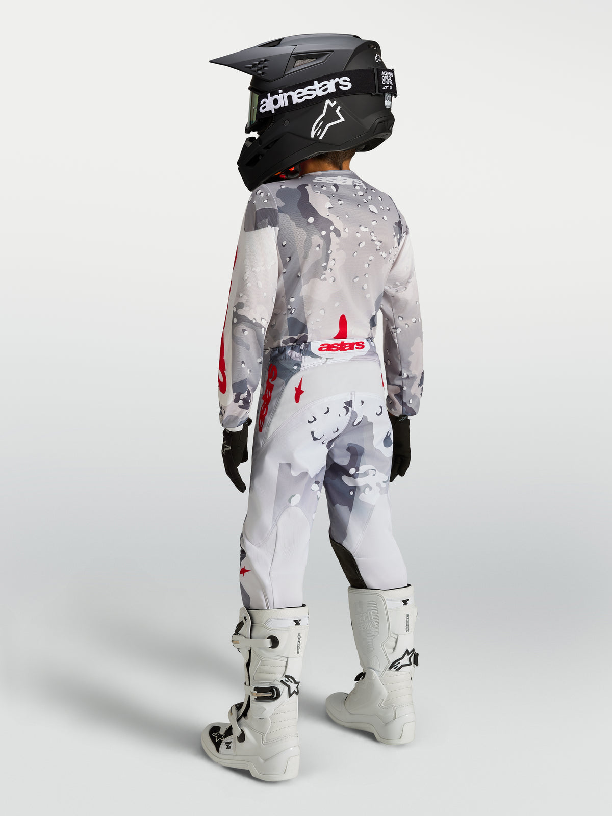 Alpinestars Youth Fluid Lone Pants, gray camo and white motocross gear with red accents, shown on a youth rider from behind.