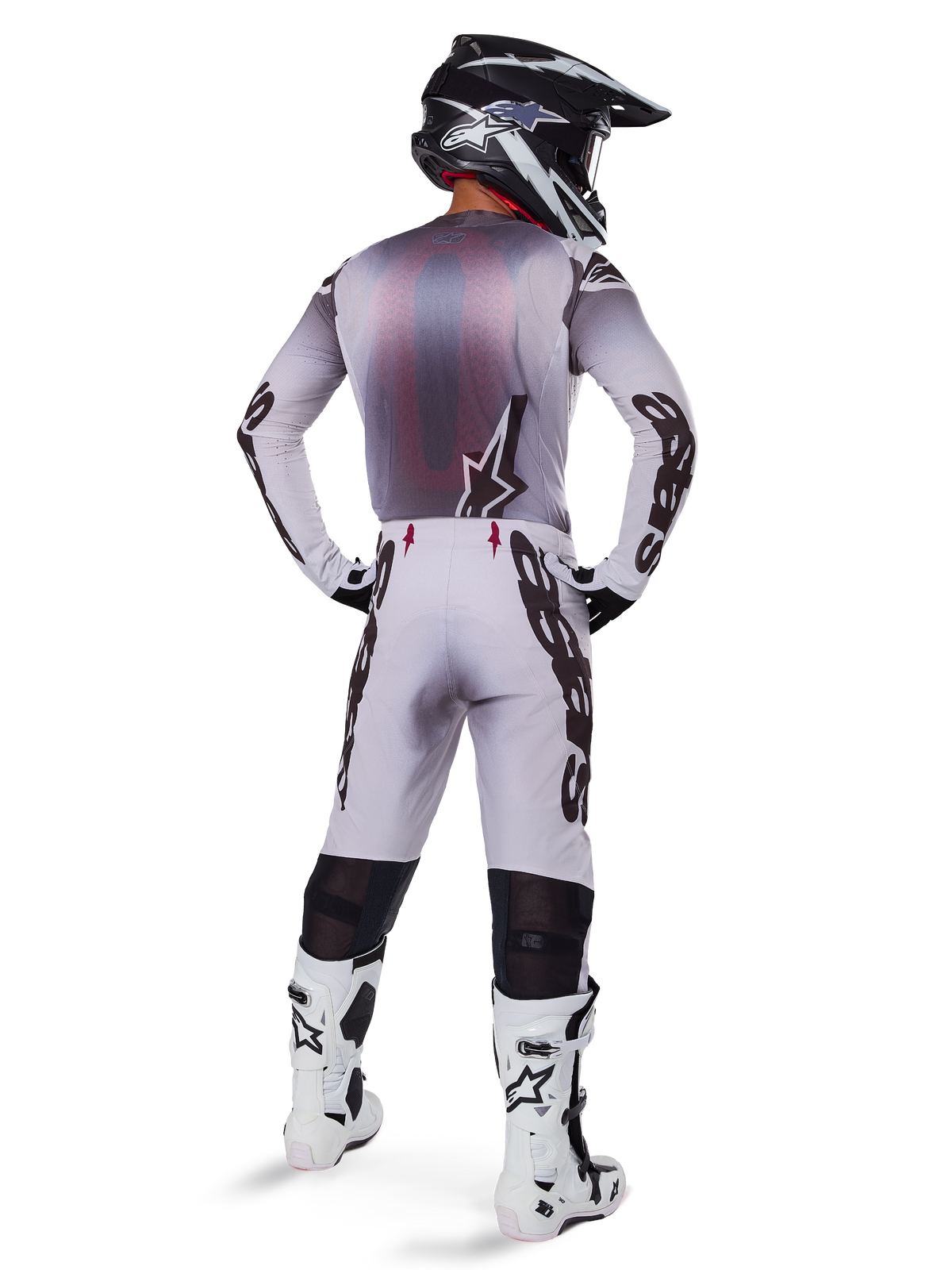 Motocross rider from behind wearing Alpinestars 2025 Supertech Maker Pants in Silver and Black, matching long-sleeve jersey, black and white helmet, and white and black boots, featuring bold black branding on the legs, professional off-road racing gear.