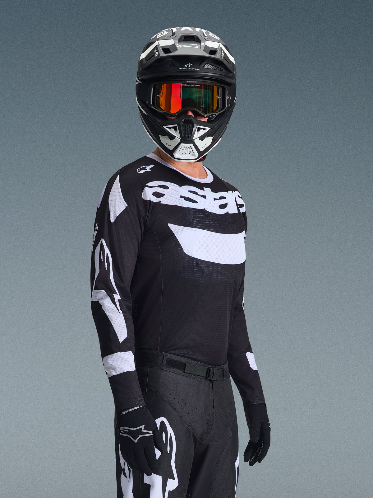 Piloto de motocross a usar a Camisola Racer Air Riway 2026, camisola preta e branca com o logótipo 'astars', capacete preto e branco a condizer com óculos espelhados cor de laranja, calças e luvas de motocross pretas, conjunto coordenado para todo-o-terreno