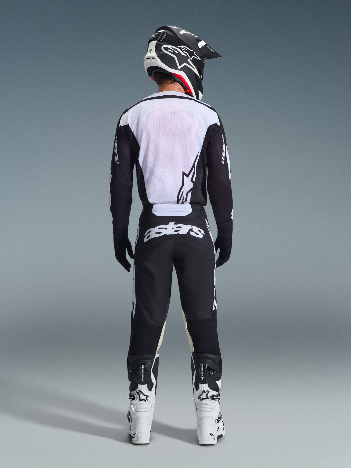 Alpinestars 2026 Racer Air Riway Gear Set, equipamento de motocross, preto e branco, vista traseira de piloto com camisola ventilada e painéis de malha brancos, calças a condizer com logótipo astars em destaque no assento, coordenado com botas e capacete de motocross brancos e pretos
