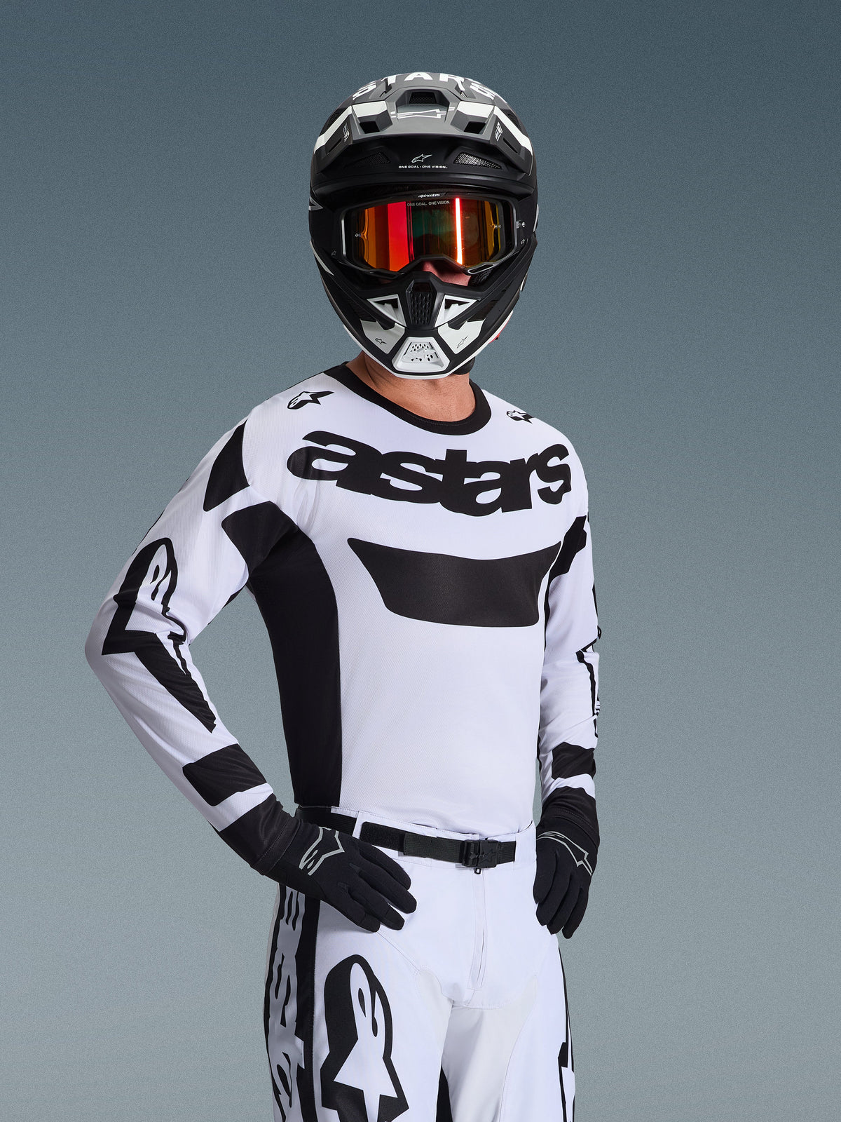 Alpinestars 2026 Racer Riway Jersey, camisola de motocross, branca e preta, com logótipo 'astars' em destaque no peito, usada com calças brancas a condizer e luvas pretas, capacete preto e branco com óculos refletores vermelhos, equipamento profissional de corrida todo-o-terreno