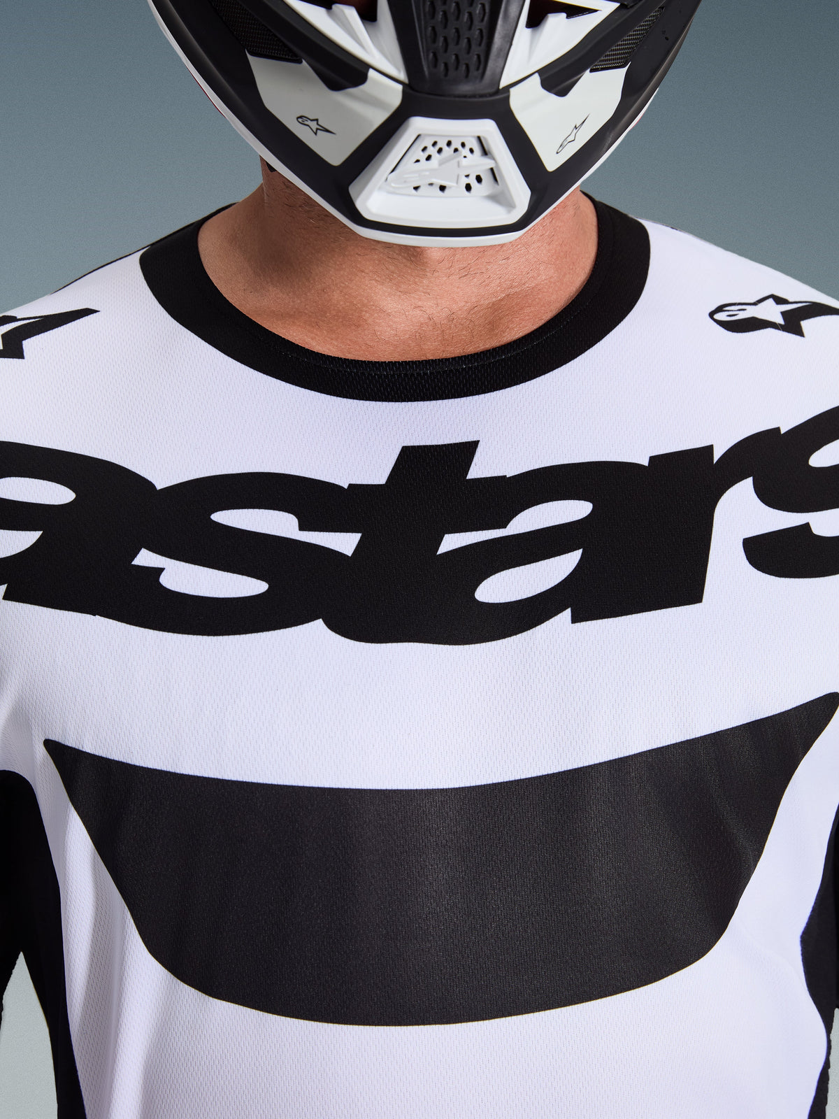 Alpinestars 2026 Racer Riway Jersey, camisola de motocross, branca e preta, grande plano do peito com logótipo astars preto em destaque e gola preta, usada com capacete branco e preto, equipamento de condução todo-o-terreno de alta performance
