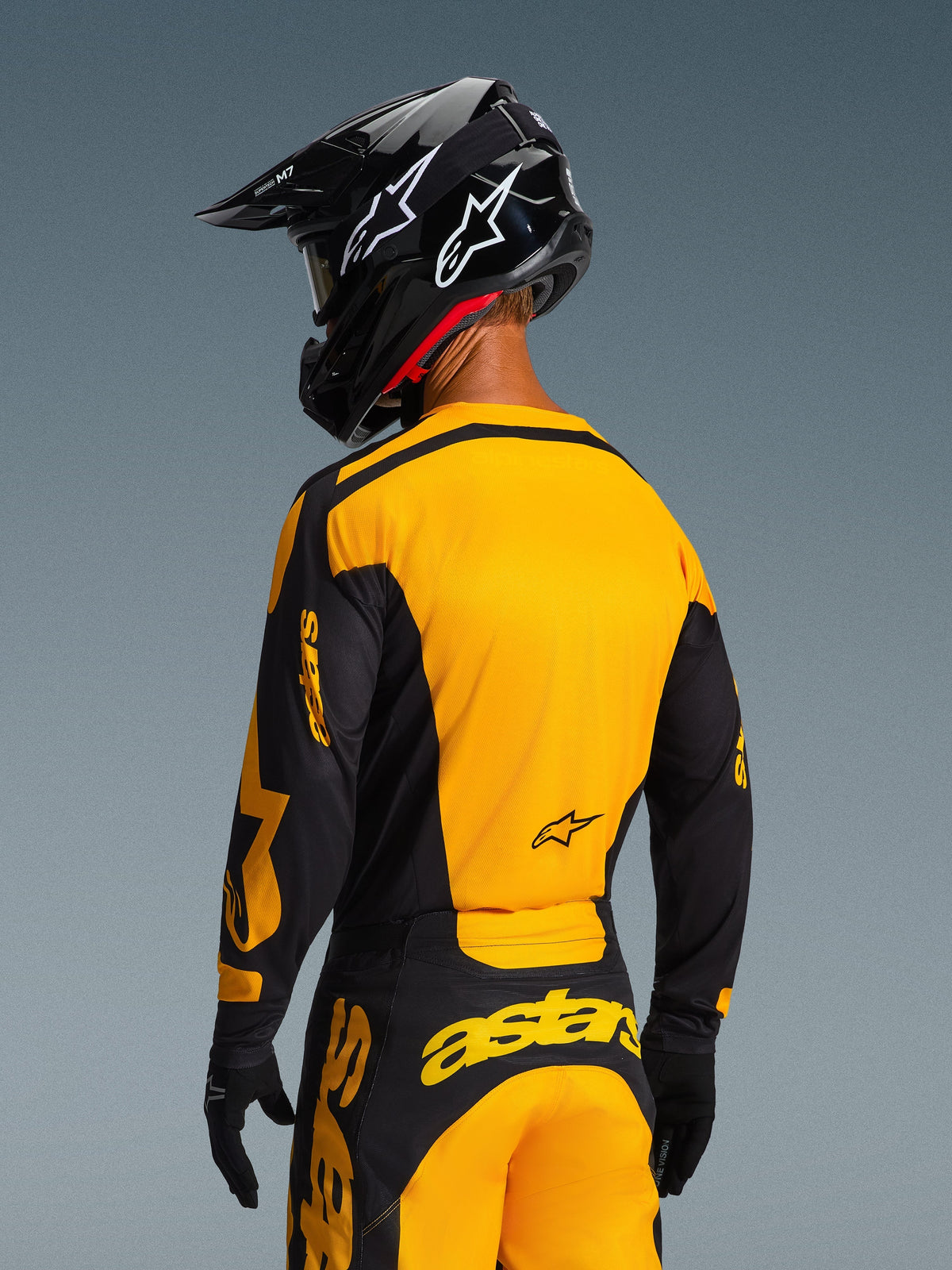 Motocross rider from behind wearing the 2026 Racer Riway Jersey and matching pants in Yellow and Black, featuring bold Alpinestars branding, black helmet with white star logos, and black gloves, coordinated motocross gear set for off-road racing.
